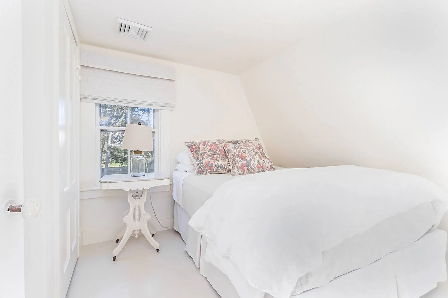 Dormer bedroom with white bedding and floral pillows highlights a cozy Cape Cod cottage renovation.