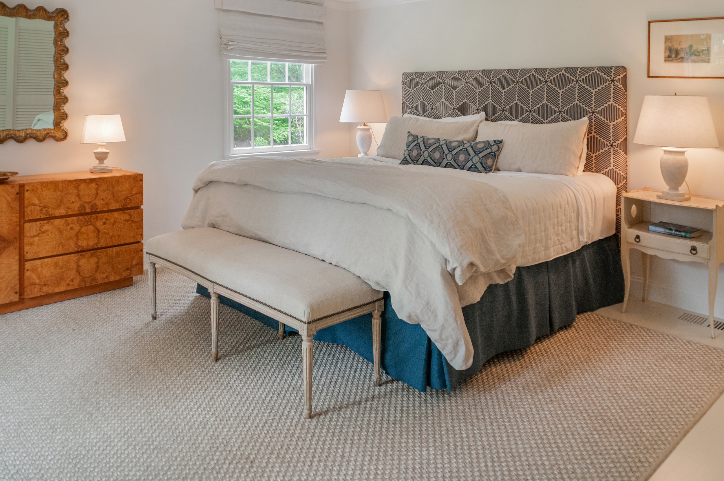 Layered bedding and upholstered headboard define this Cape Cod bedroom renovation with coastal home styling.