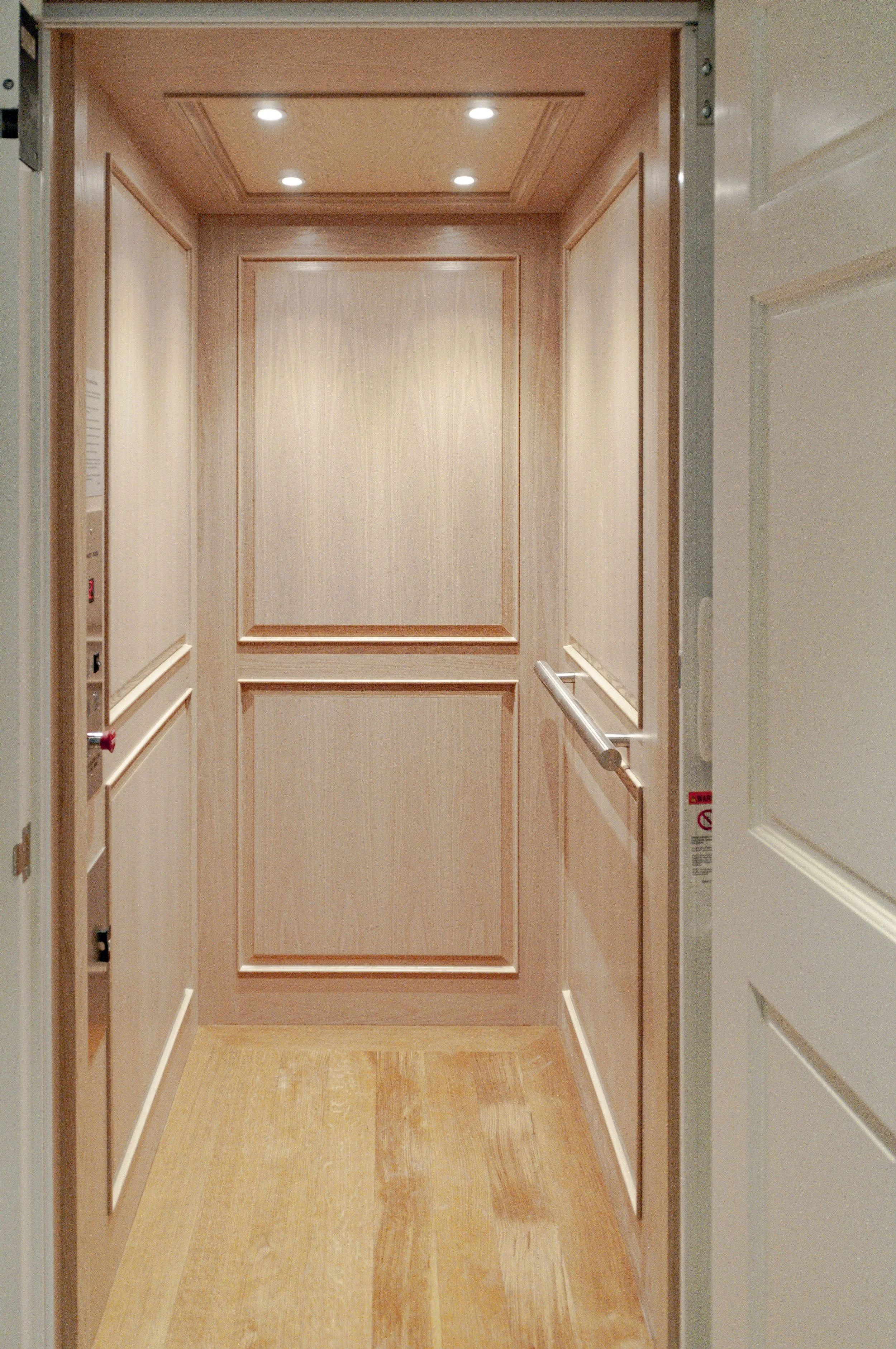 Custom home elevator with wood paneling, recessed lighting, handrails, and polished Cape Cod craftsmanship.