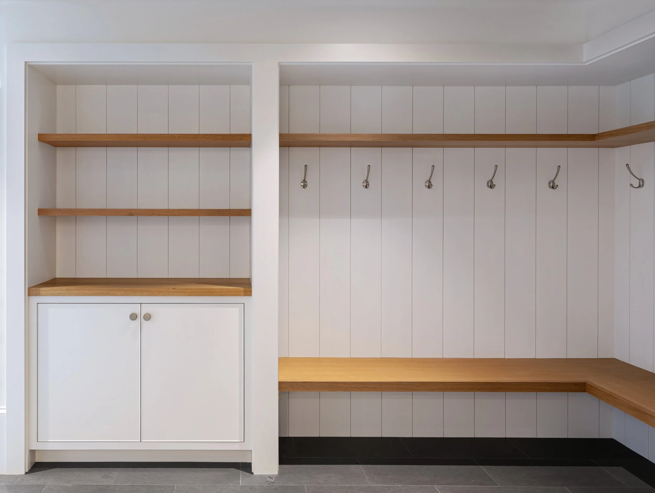 Thoughtfully designed mudroom featuring custom cubbies, wood bench seating, built-in cabinetry, and coat hooks for functional Cape Cod home organization.