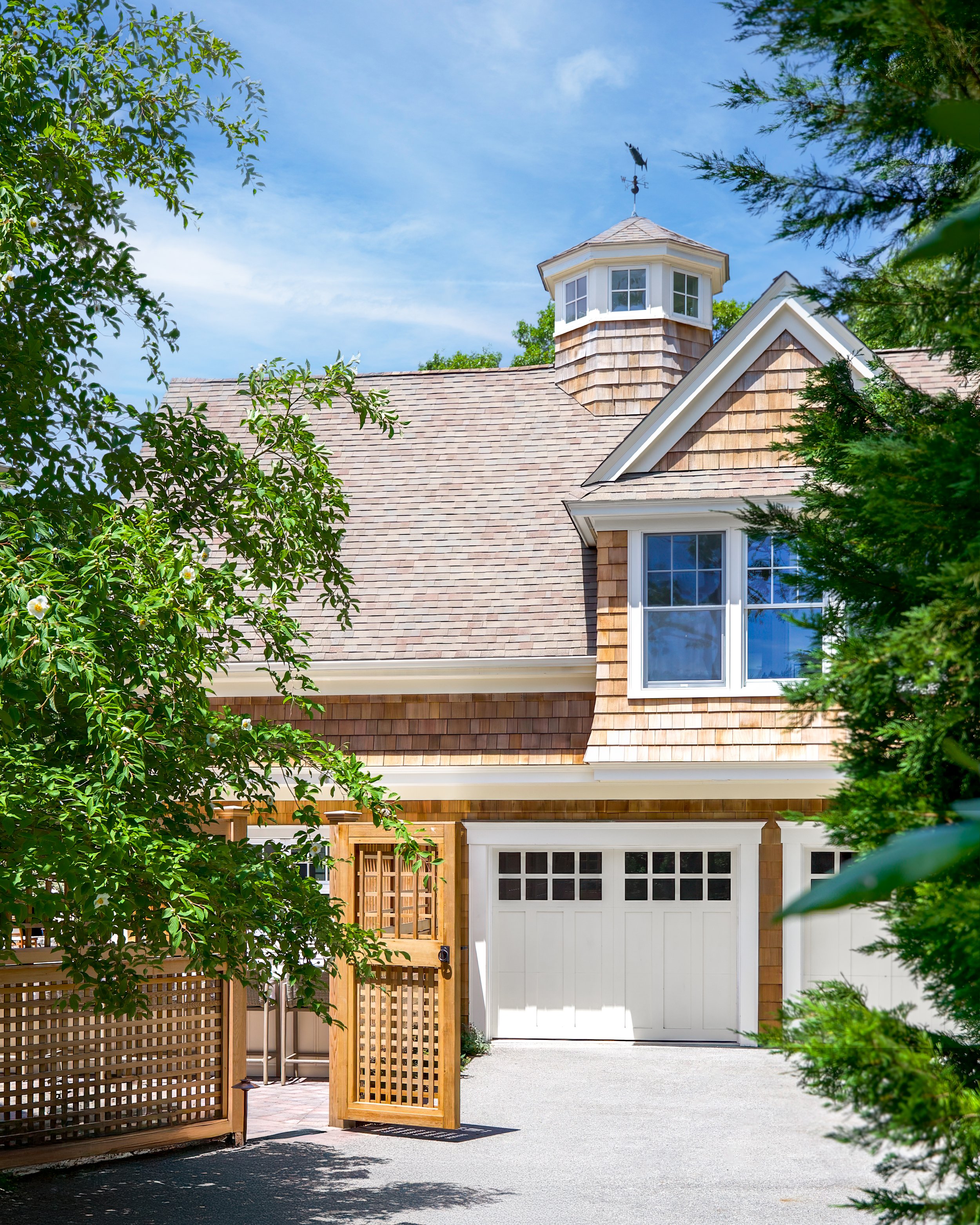Cedar-shingled exterior, cupola, garage doors, and lattice gate create classic Cape Cod curb appeal.