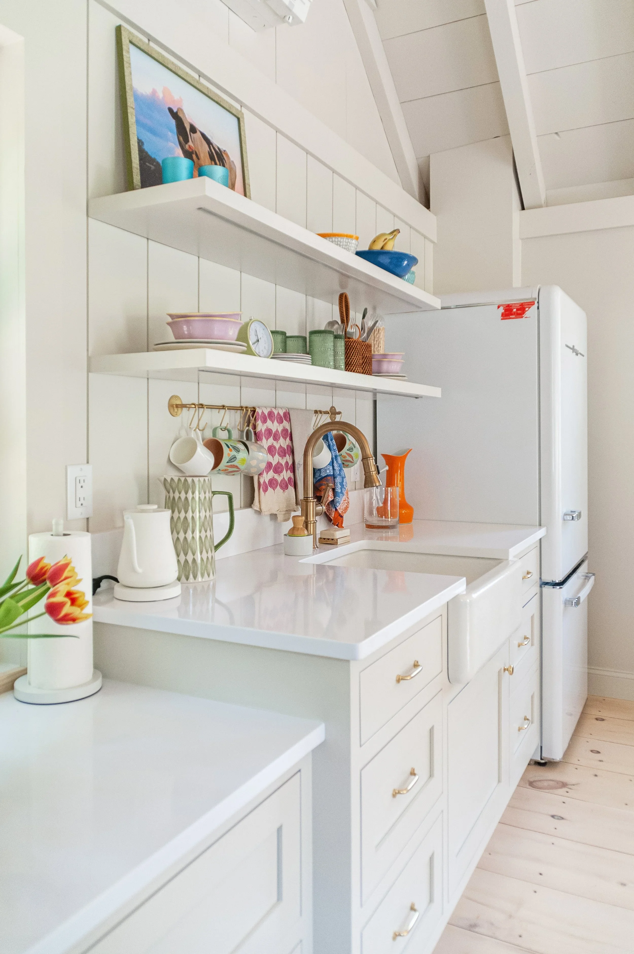 Open shelving and custom cabinetry create a functional Cape Cod pool house kitchenette with quartz countertops, brass fixtures, and built-in storage.