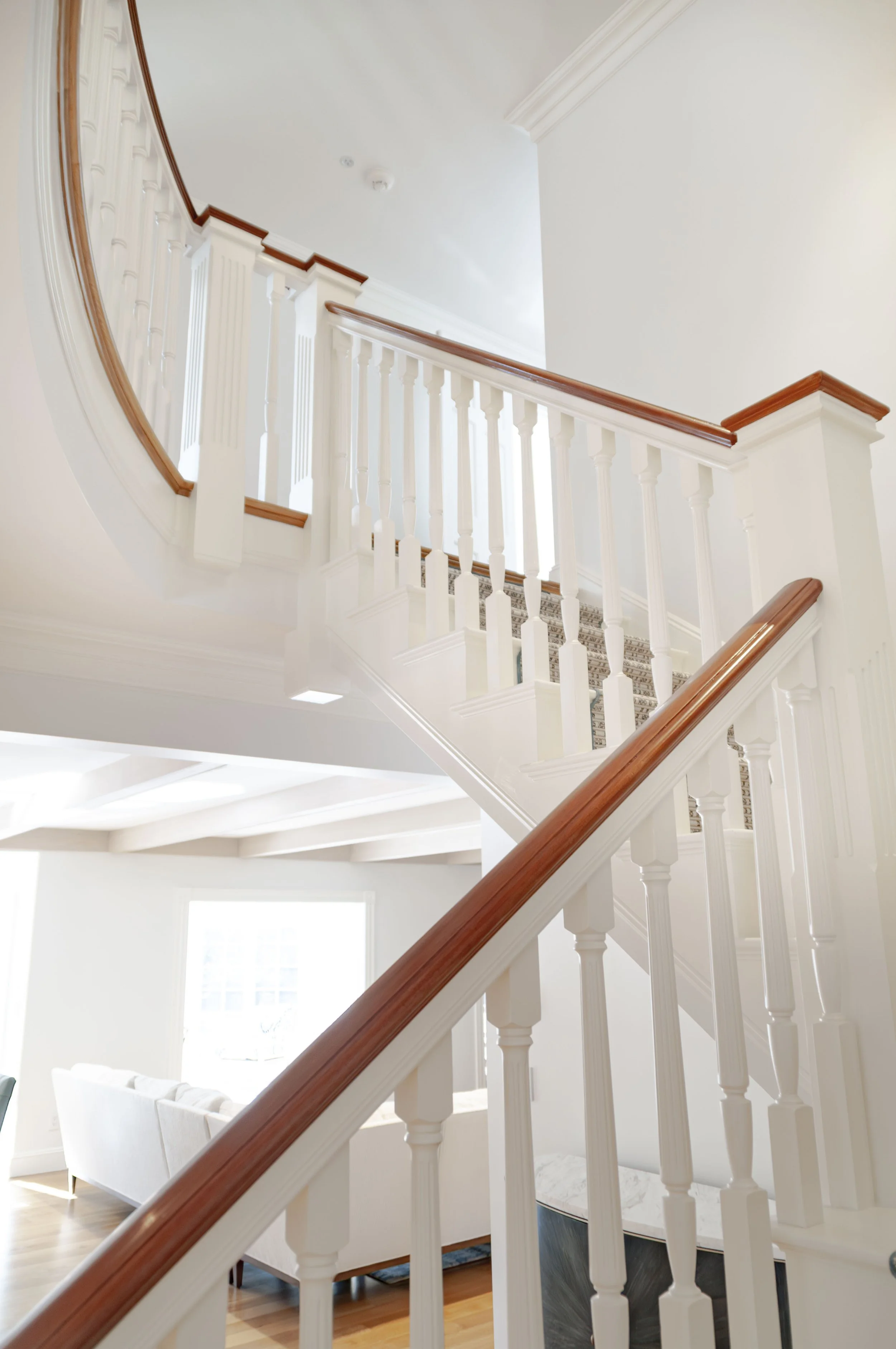 Staircase with white balusters, wood handrails, curved landing, and bright open interior.