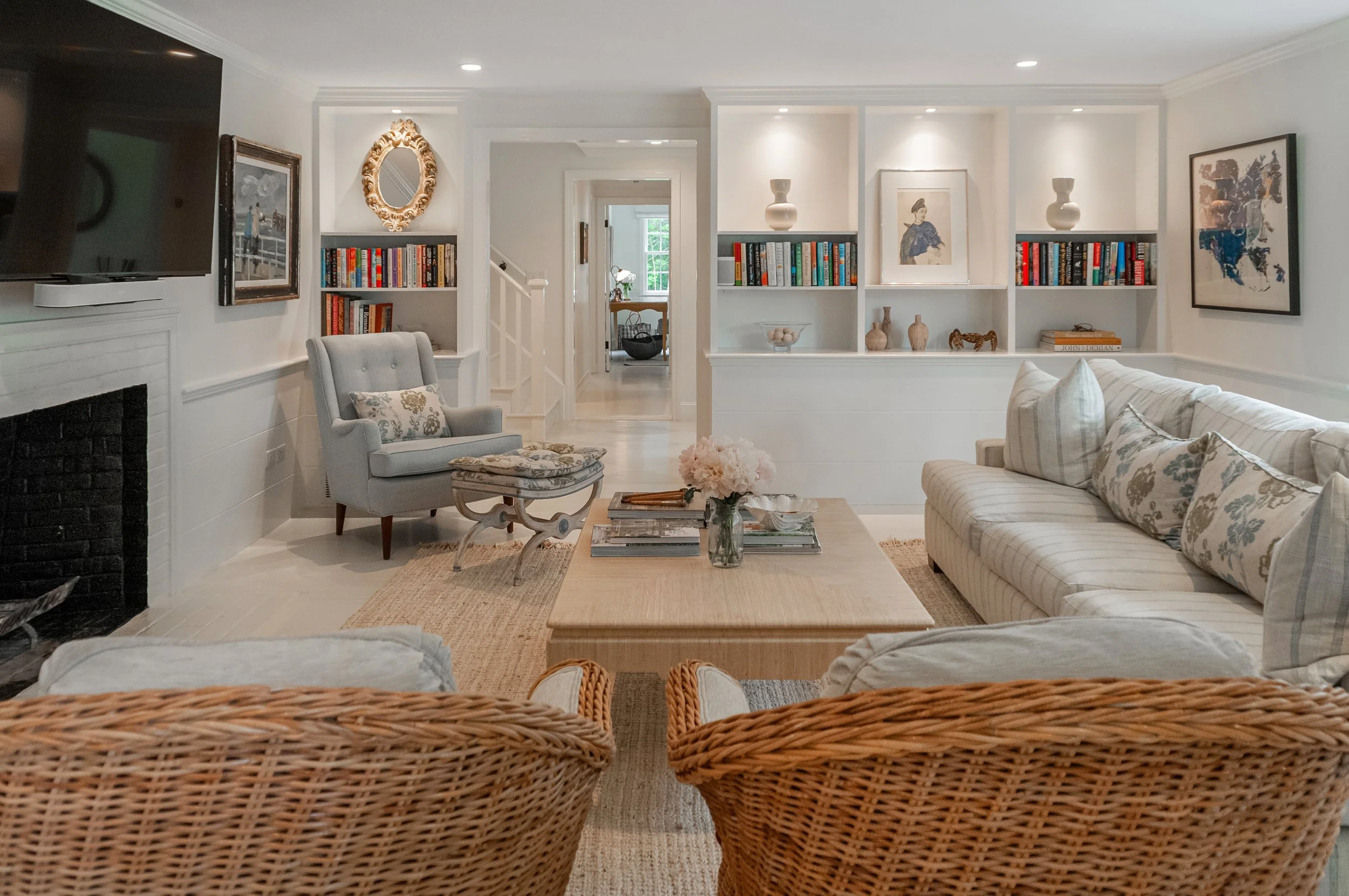 Built-in shelving, fireplace seating, and woven chairs bring refined Cape Cod interiors to this living room.