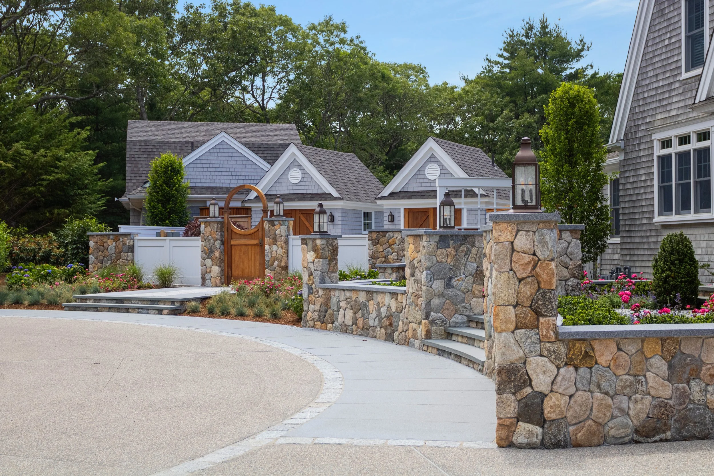 Stone walls and lush landscaping frame a shingle-style Cape Cod home with custom coastal charm.