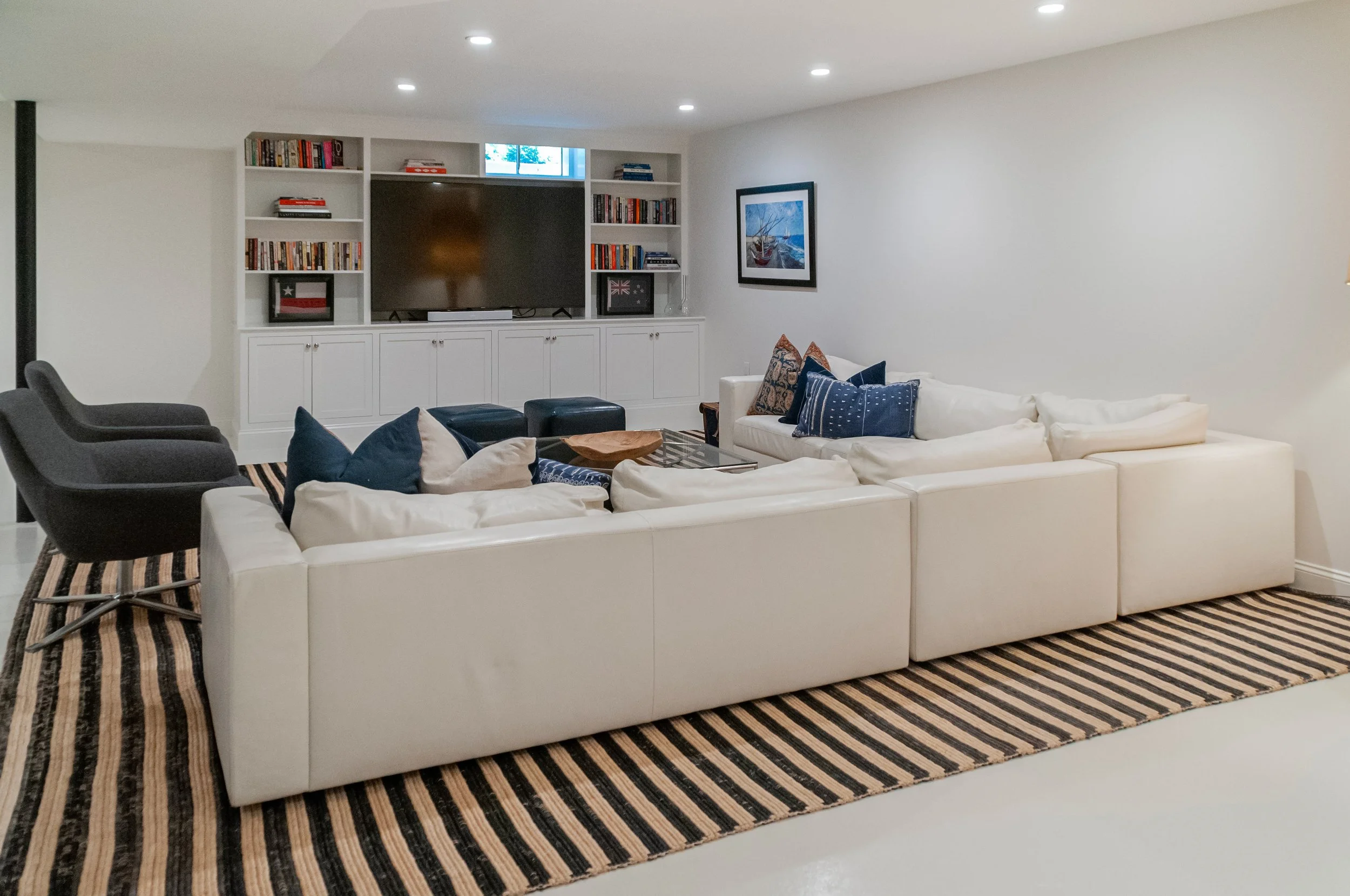 Lower-level lounge in a custom Cape Cod home with sectional seating, built-ins, and striped rug.