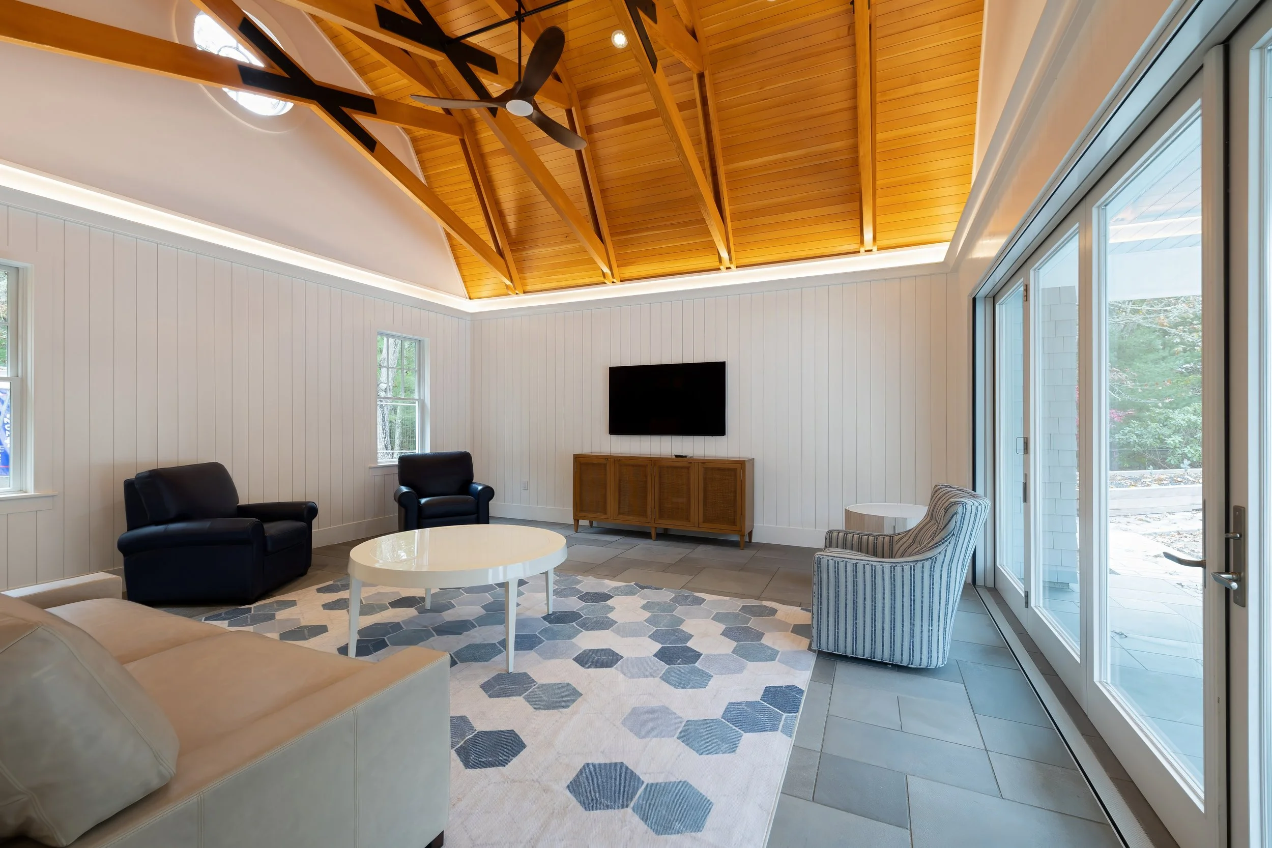 Bright pool house living room with wood-beamed ceiling, glass doors, and coastal furnishings.