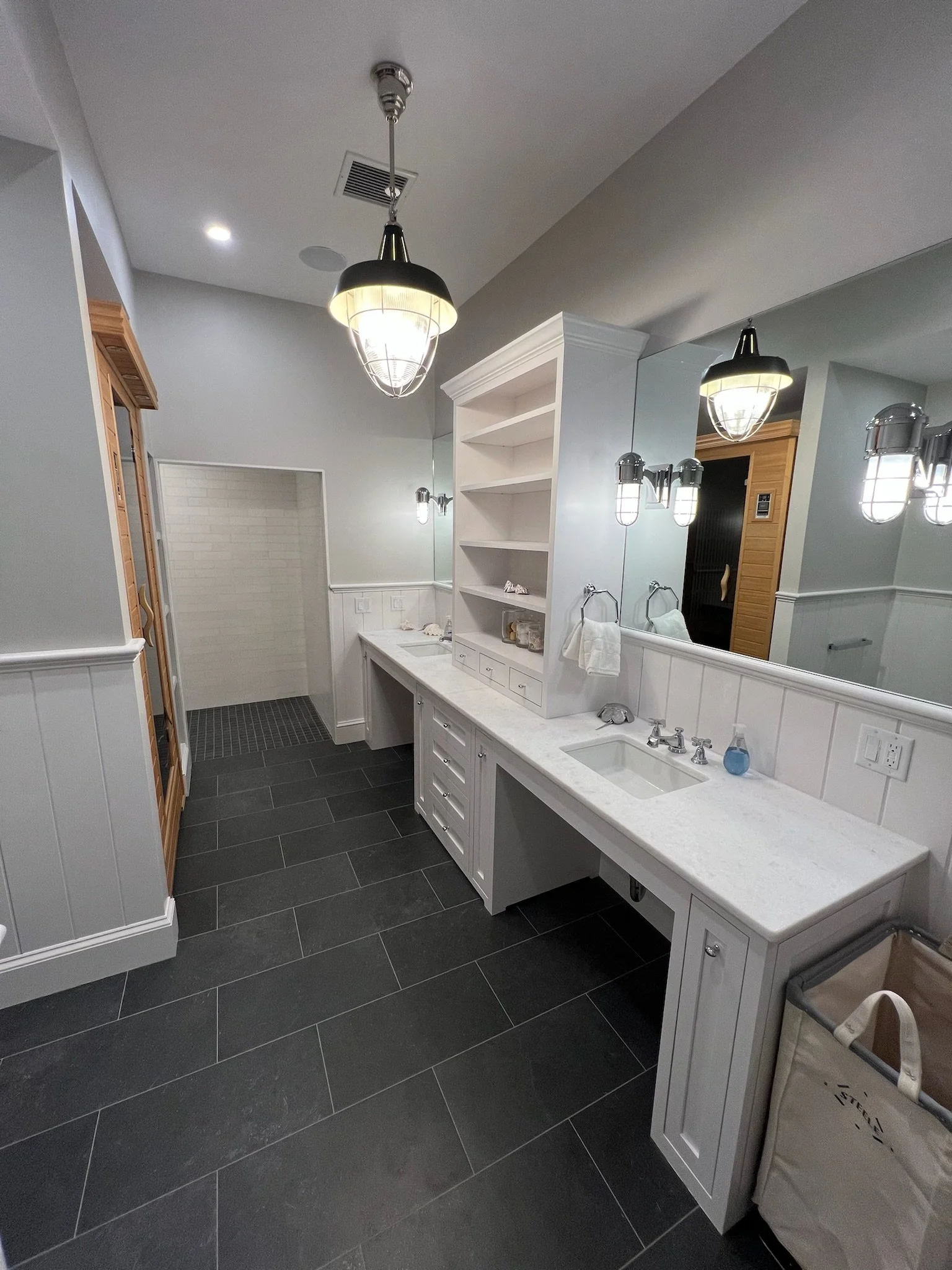 Built-in shelving and dark tile floors give this custom coastal home bath a refined functional layout