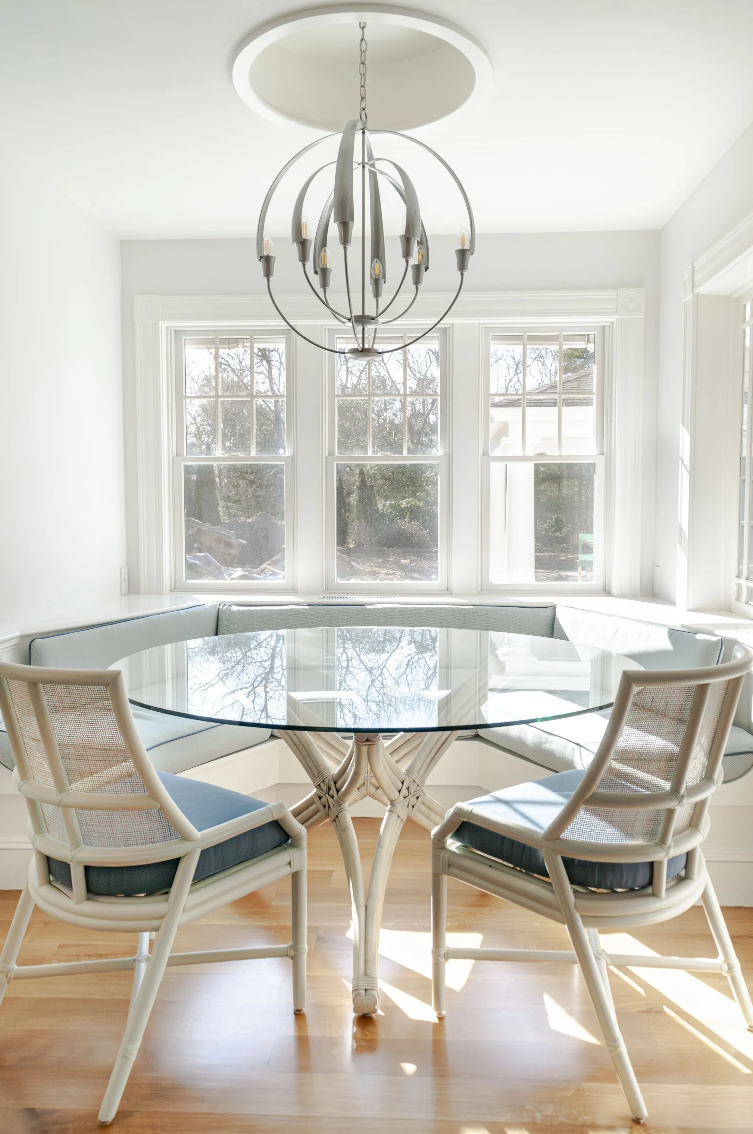 Designed for everyday dining, this Sea View Builders breakfast nook features a custom banquette, expansive windows, designer lighting, and timeless Cape Cod coastal style.