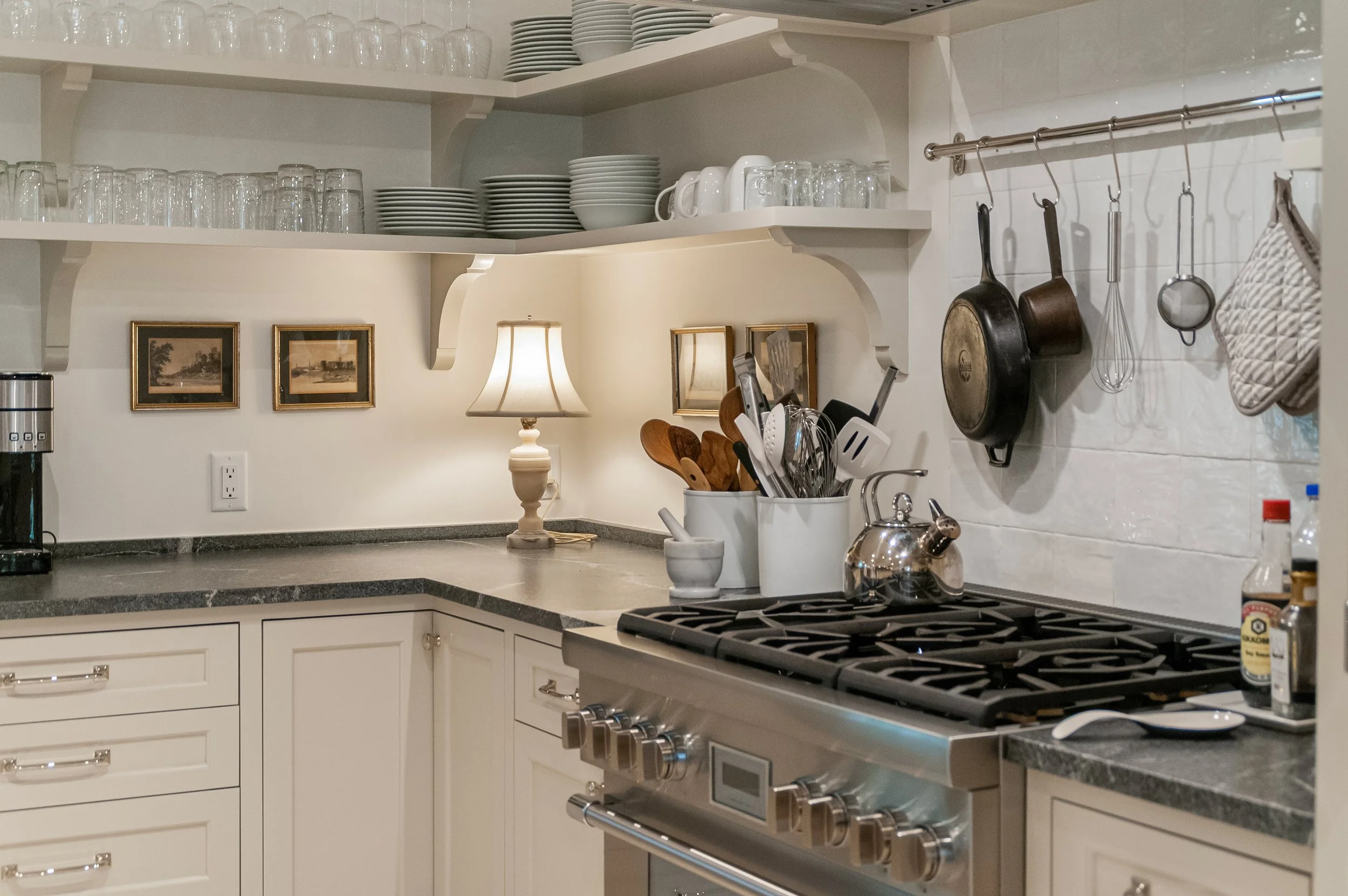 Custom Cape Cod kitchen with professional range, open dish shelving, hanging pans, and white tile backsplash.