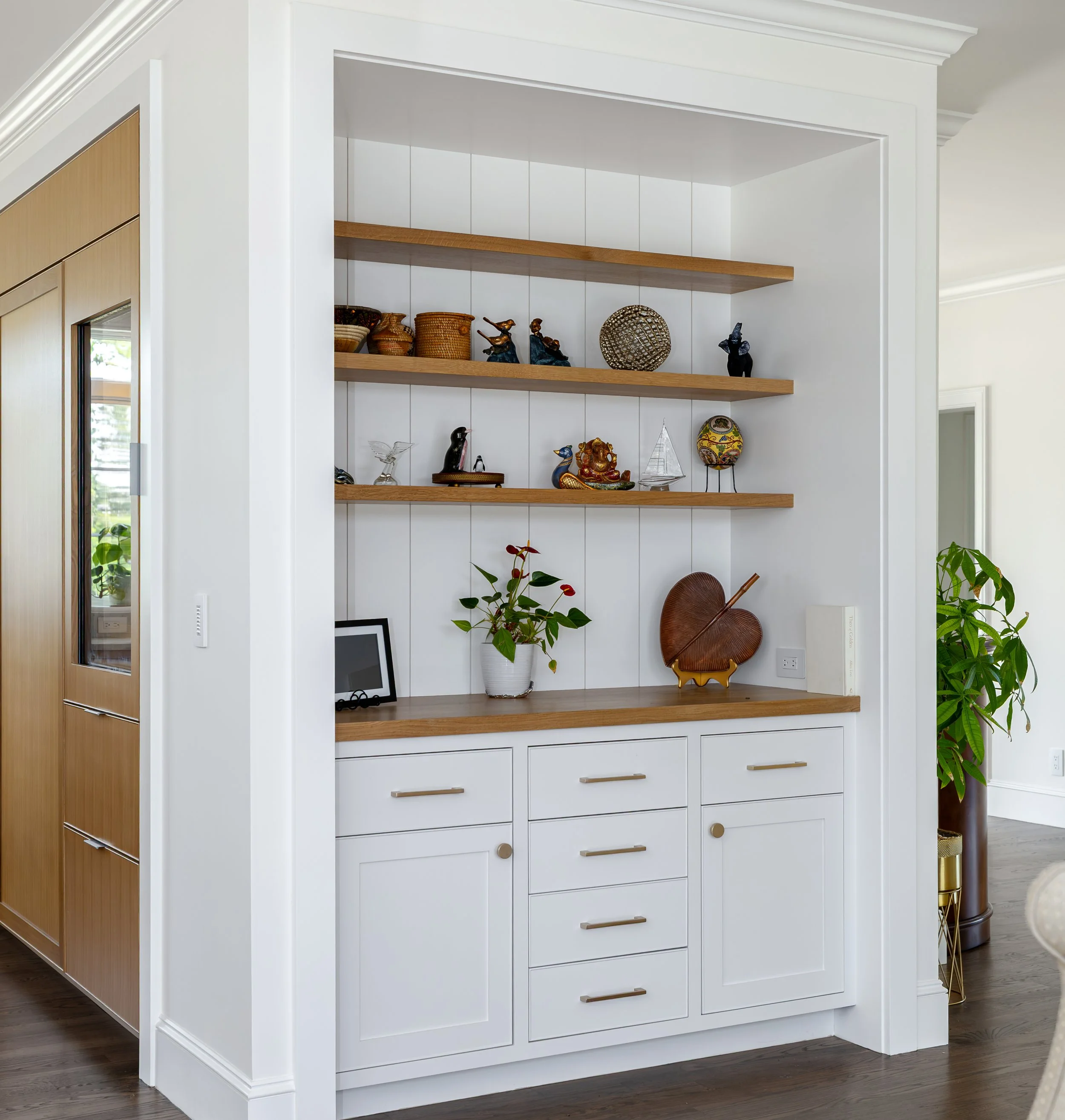 Floor-to-ceiling built-in shelving combines custom cabinetry, natural wood accents, and display storage for a bright, organized Cape Cod interior.