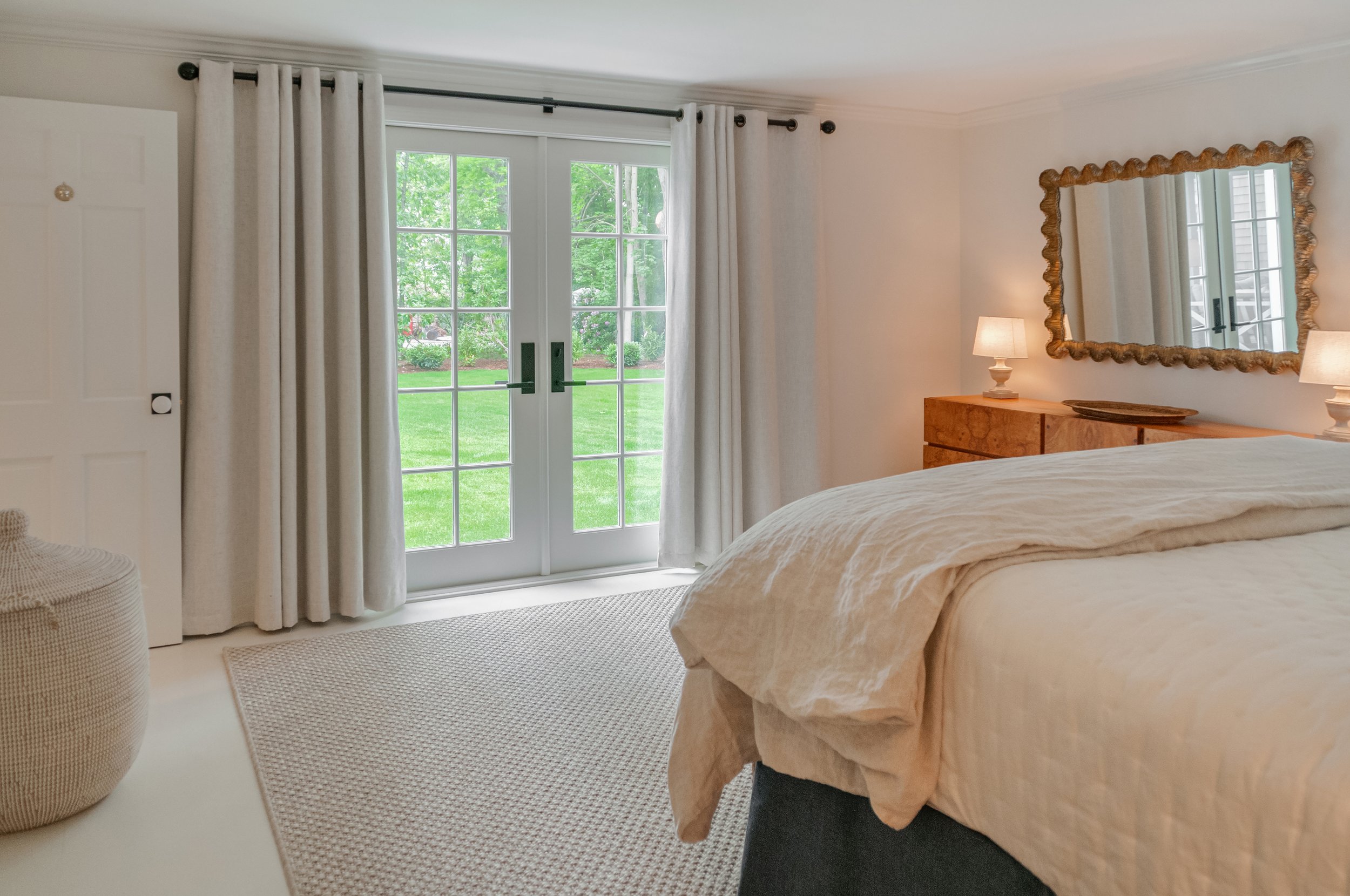 French doors, neutral bedding, and a carved wood mirror create polished coastal bedroom design.