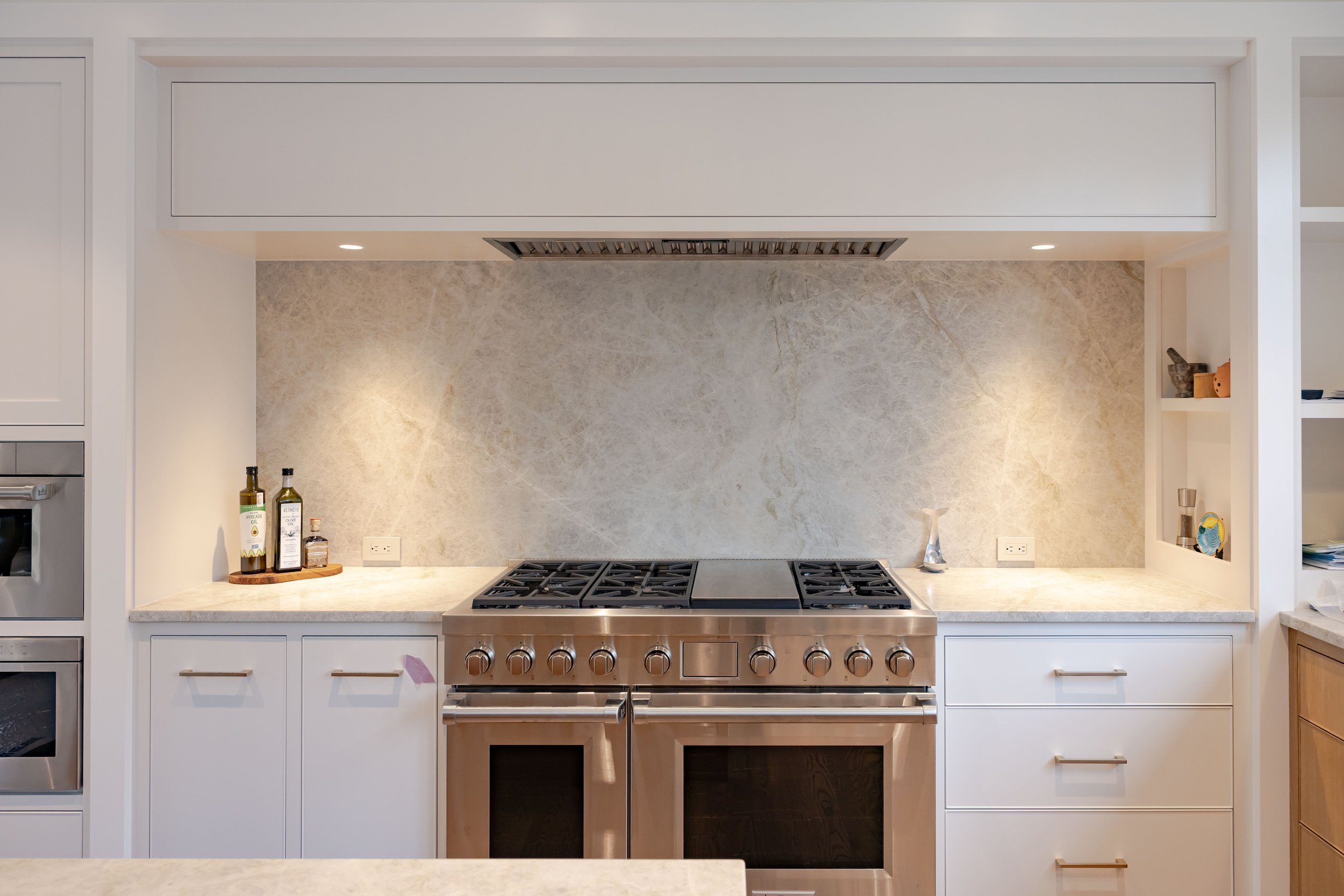 Designed for everyday cooking and entertaining, this custom kitchen features a commercial-style range, natural stone backsplash, custom cabinetry, and integrated storage.
