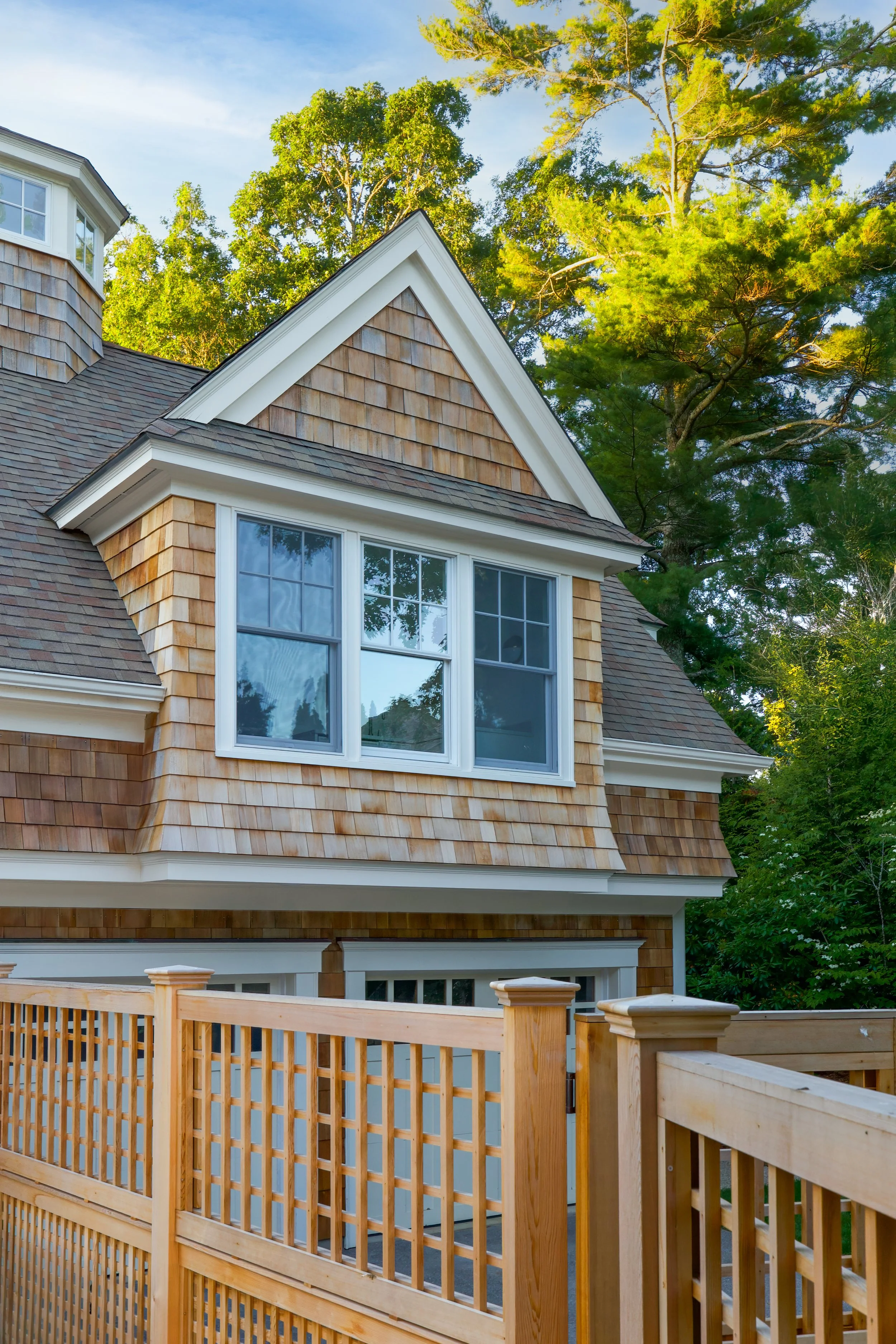 Cedar lattice and shingled dormer add texture to this Cape Cod exterior design with wooded views.