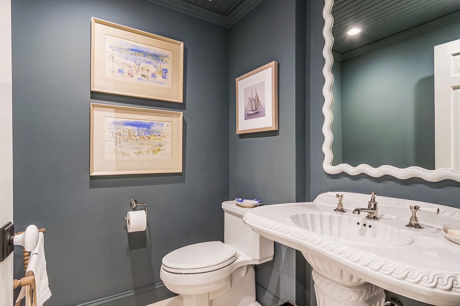 Dark painted walls and framed artwork add custom coastal home character to this detailed powder bath.