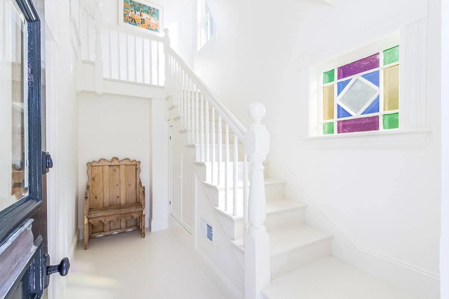 Stained glass, white staircase, and antique bench add character to this Cape Cod cottage entryway.