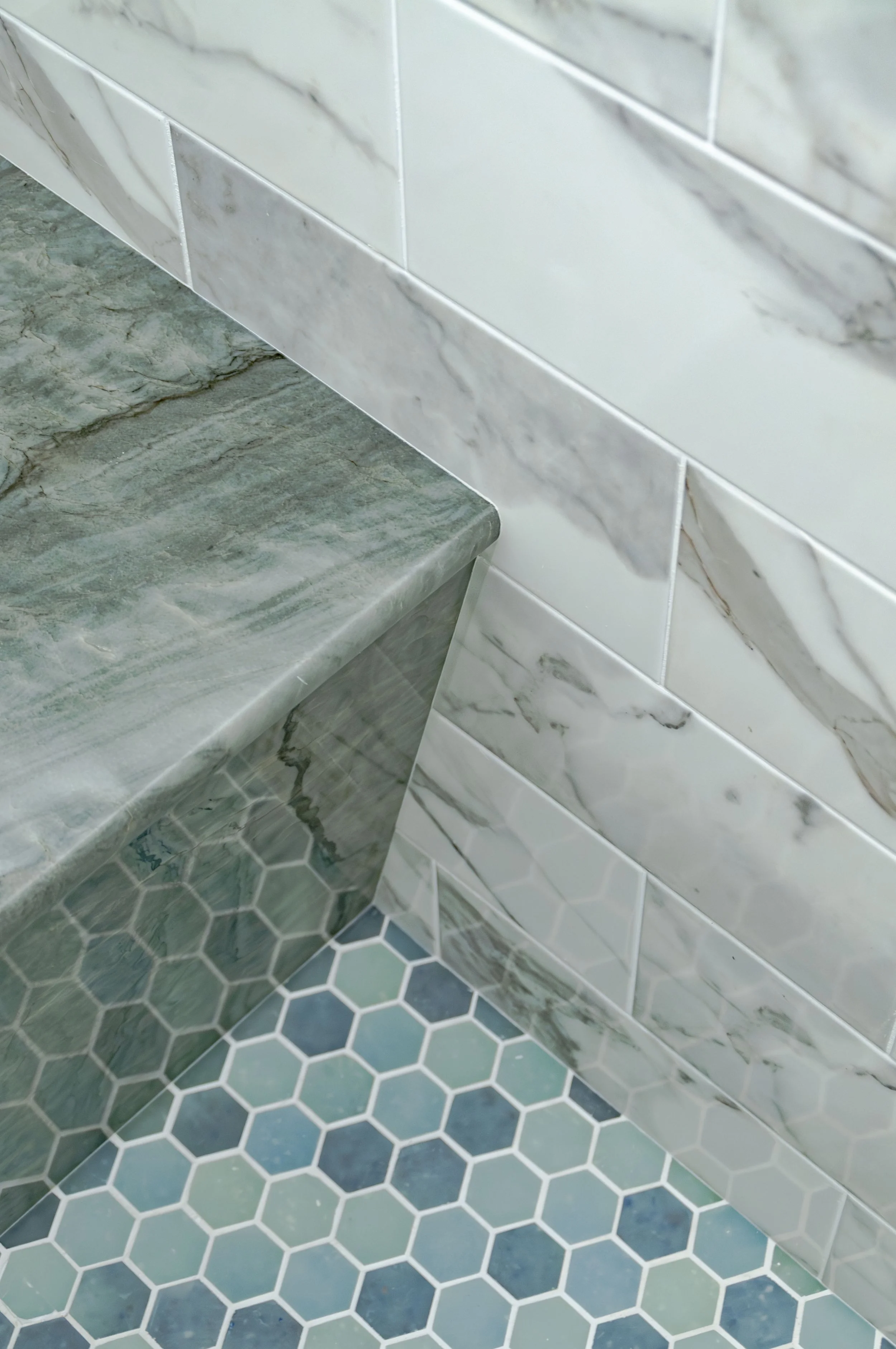 Cape Cod shower detail with blue hexagon tile, marble bench, marble-look walls, and coastal custom home finishes.