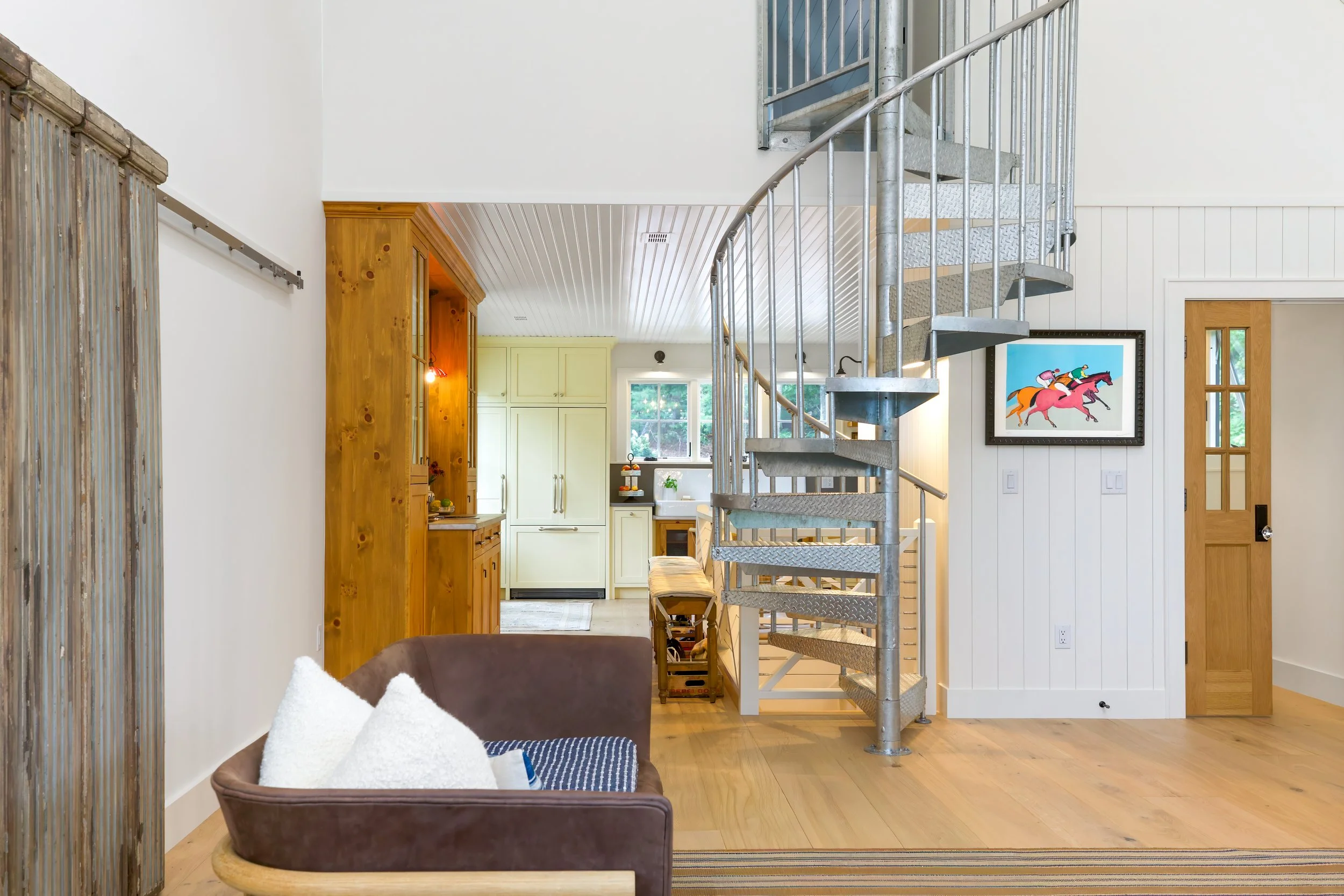 Open interior with spiral staircase, light wood floors, paneled walls, and a visible kitchen beyond.