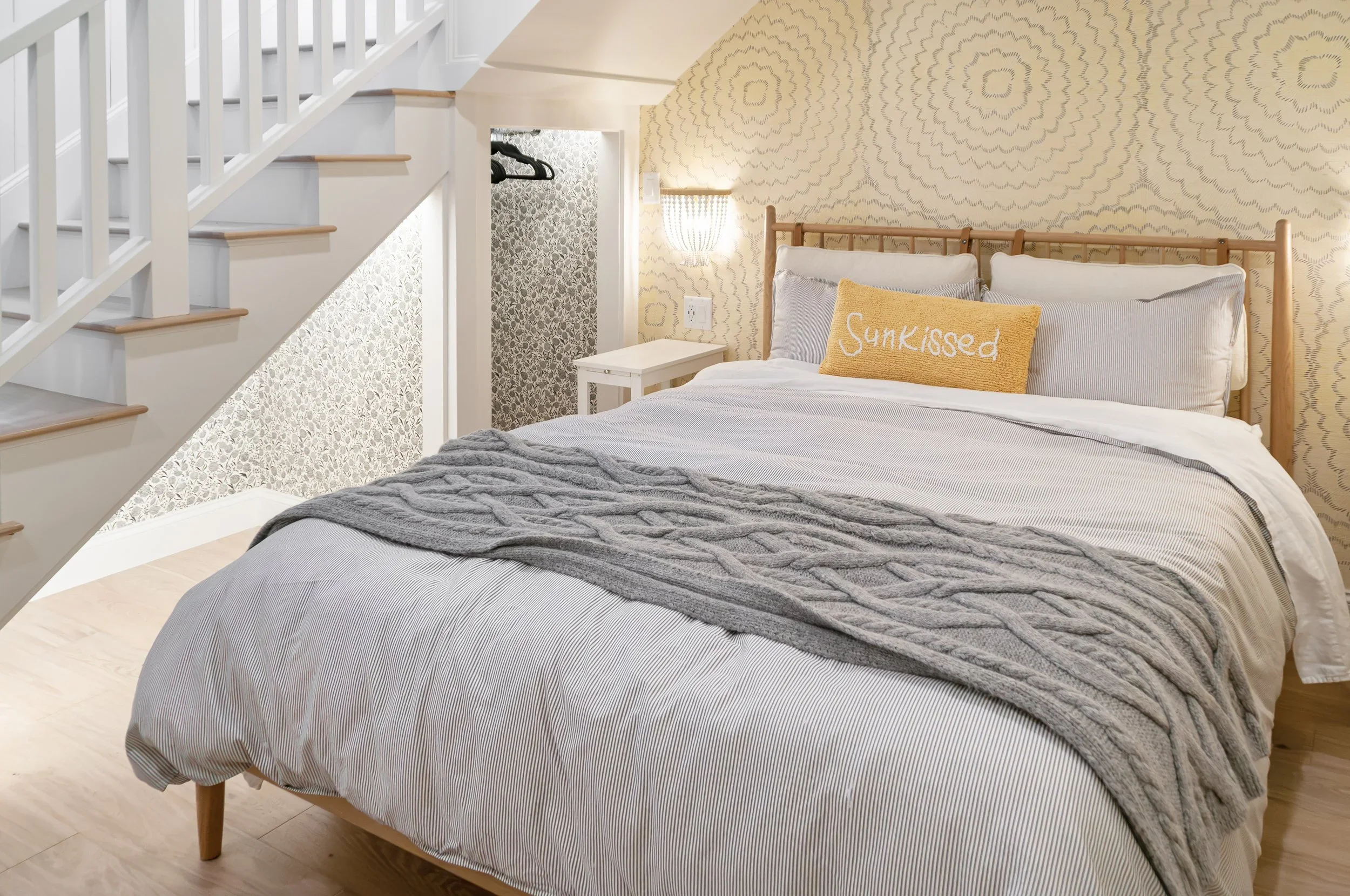 Custom guest house bedroom by Sea View Builders featuring a woven bed frame, designer wallpaper, integrated storage, and coastal Cape Cod interior design.