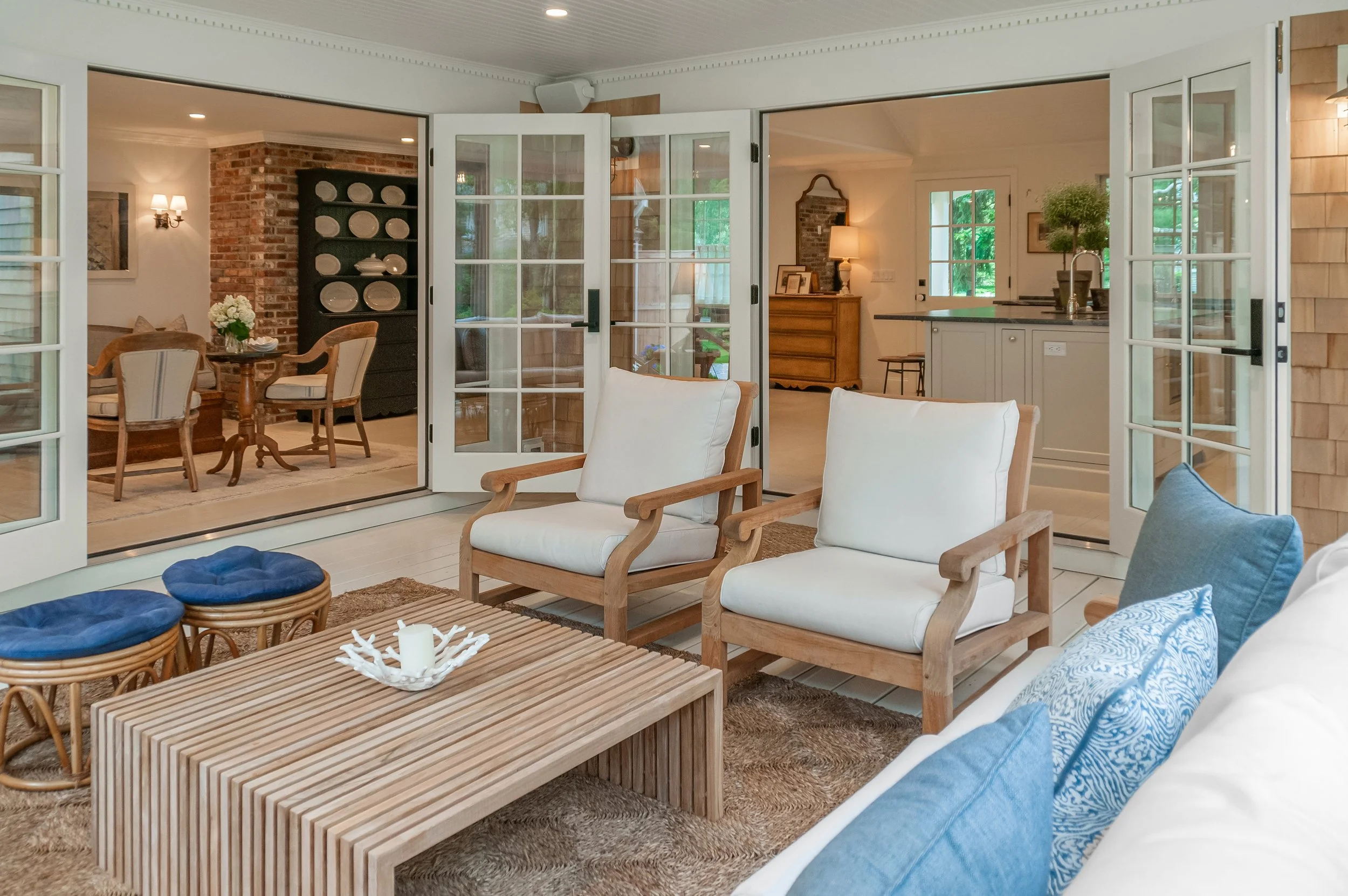 Indoor-outdoor Cape Cod living space with French doors, cushioned seating, dining area, and custom coastal finishes.