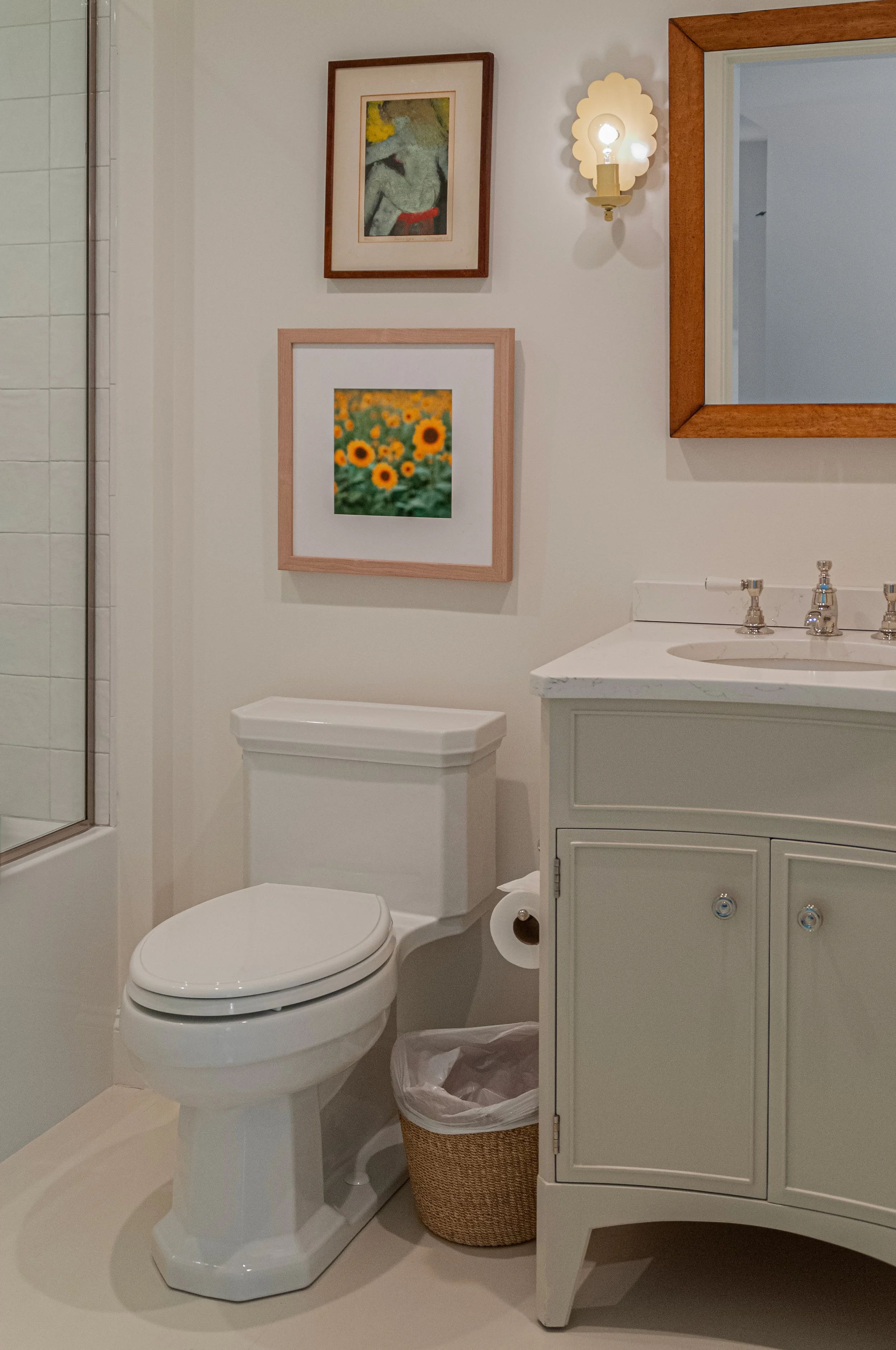 Bathroom in a Cape Cod renovation with glass shower, painted vanity, framed art, and wood mirror.