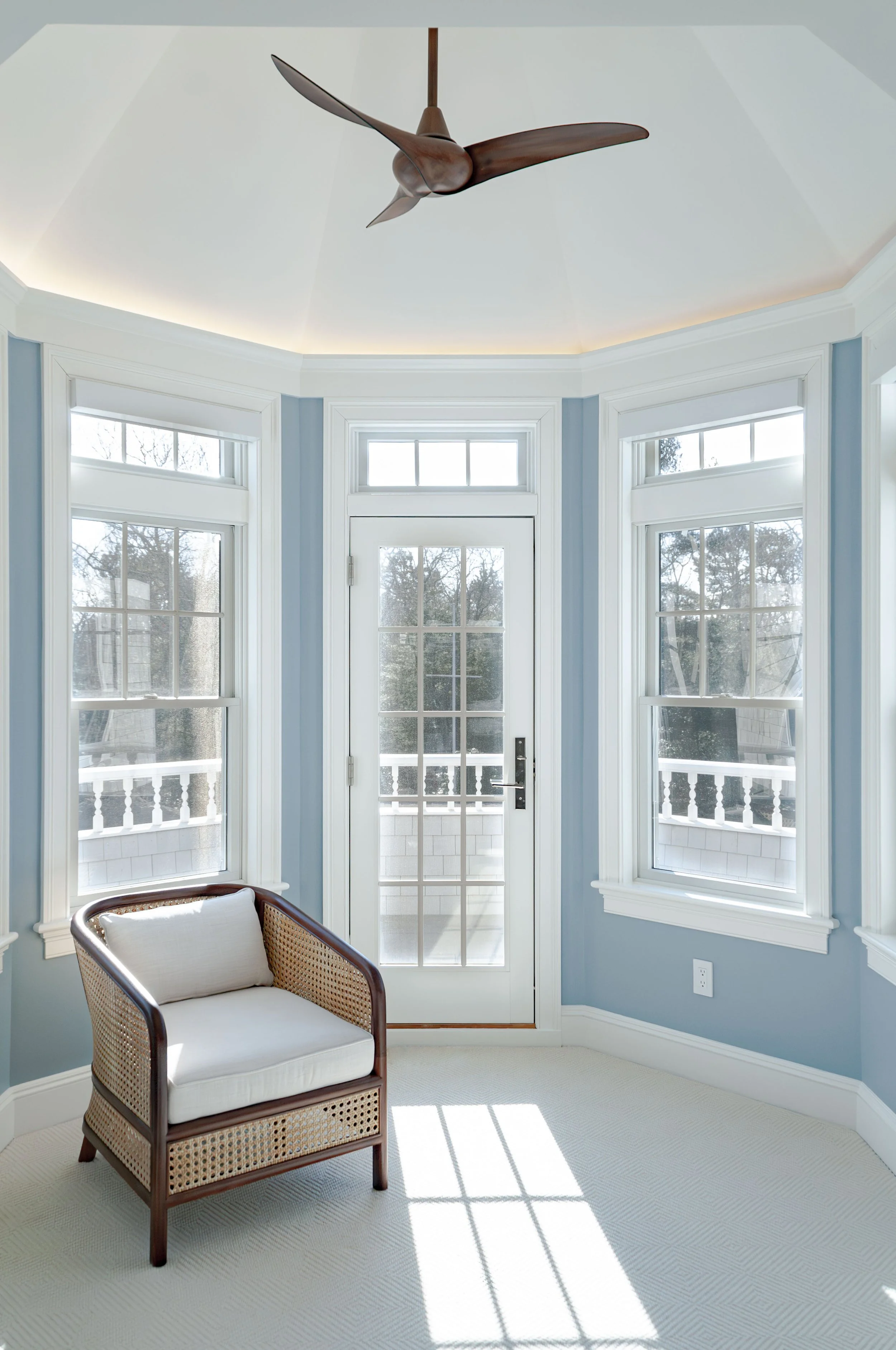 Bright Cape Cod sitting nook with blue walls, transom windows, balcony door, and custom coastal home details.