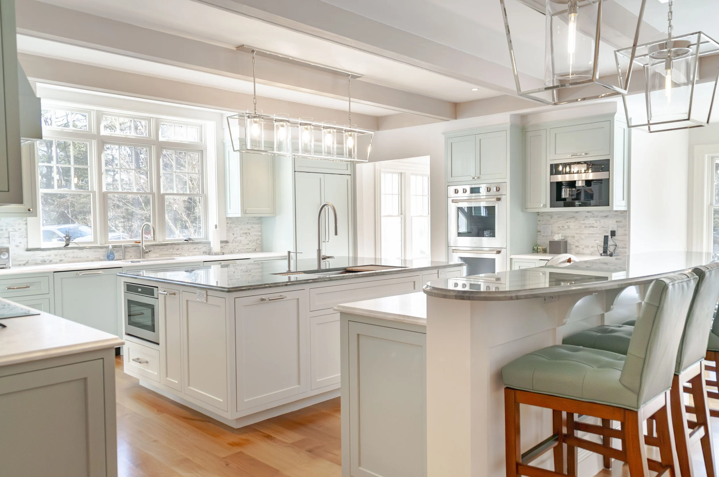 Bright Cape Cod kitchen with large island, pale cabinetry, marble counters, and upholstered counter stools.