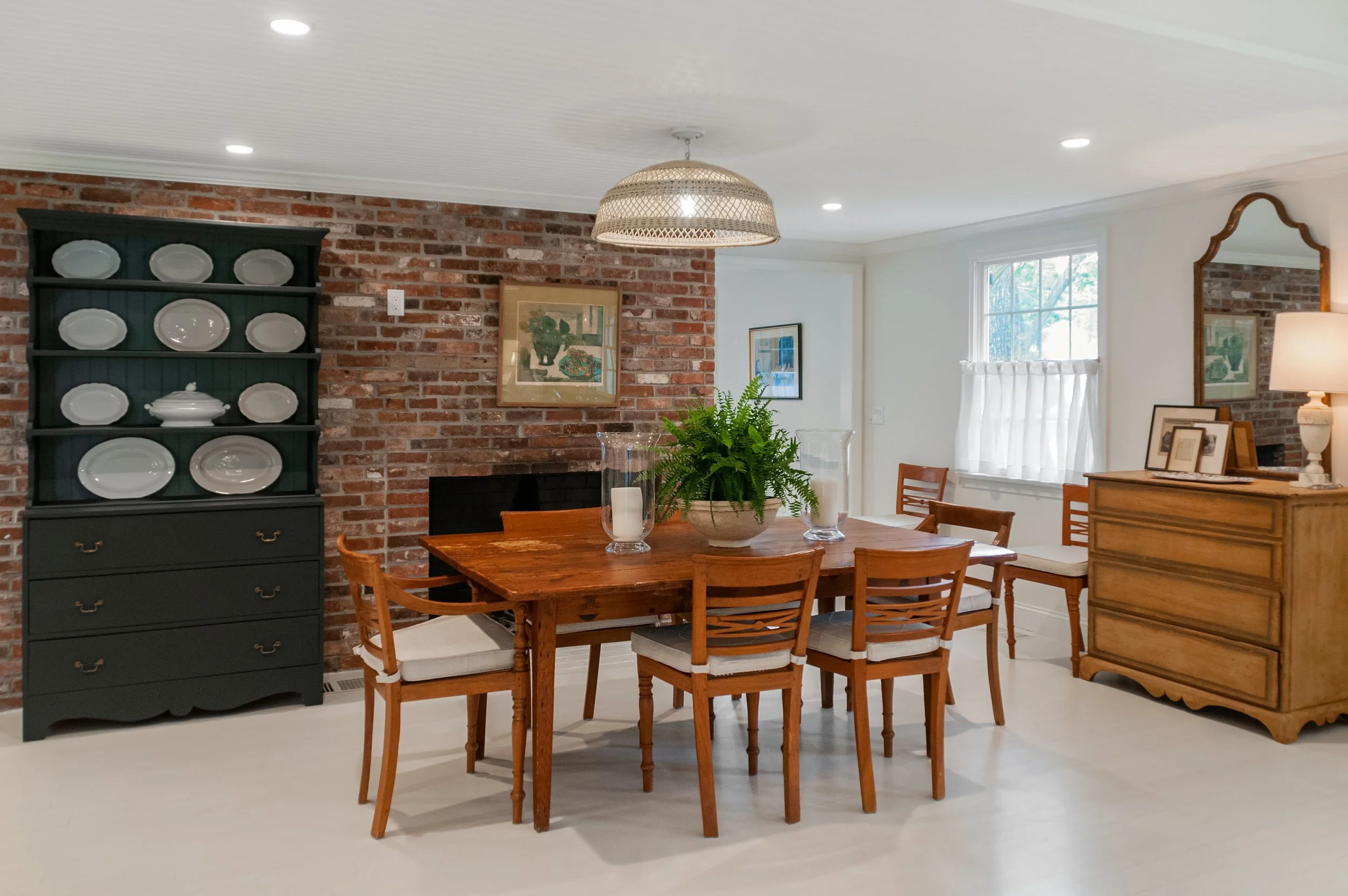 Dining room with brick fireplace wall, black plate cabinet, wood table, and custom coastal home character.