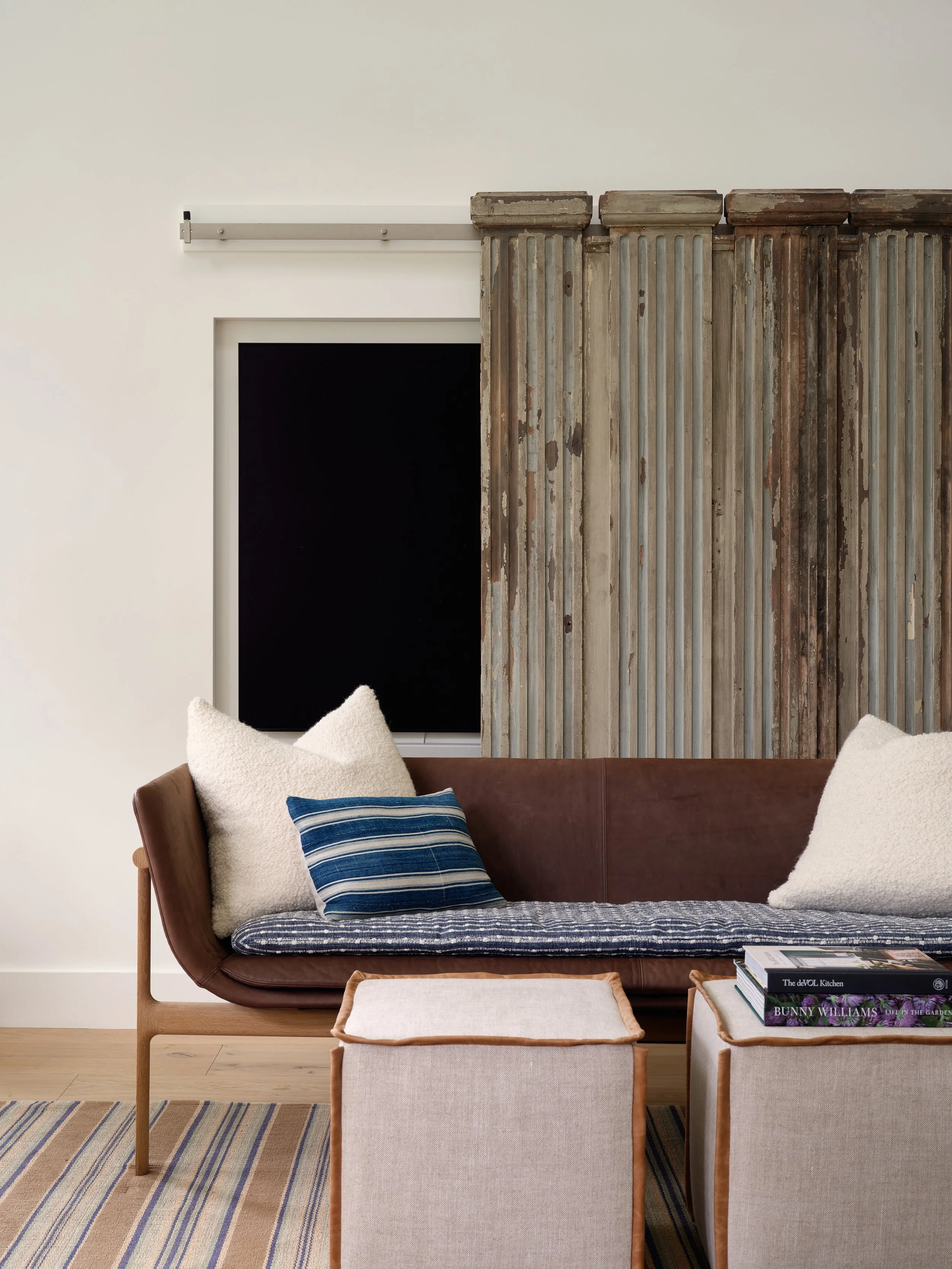 Reclaimed sliding wood doors conceal and reveal the television in this Sea View Builders living room featuring custom millwork, hardwood flooring, and timeless Cape Cod design.