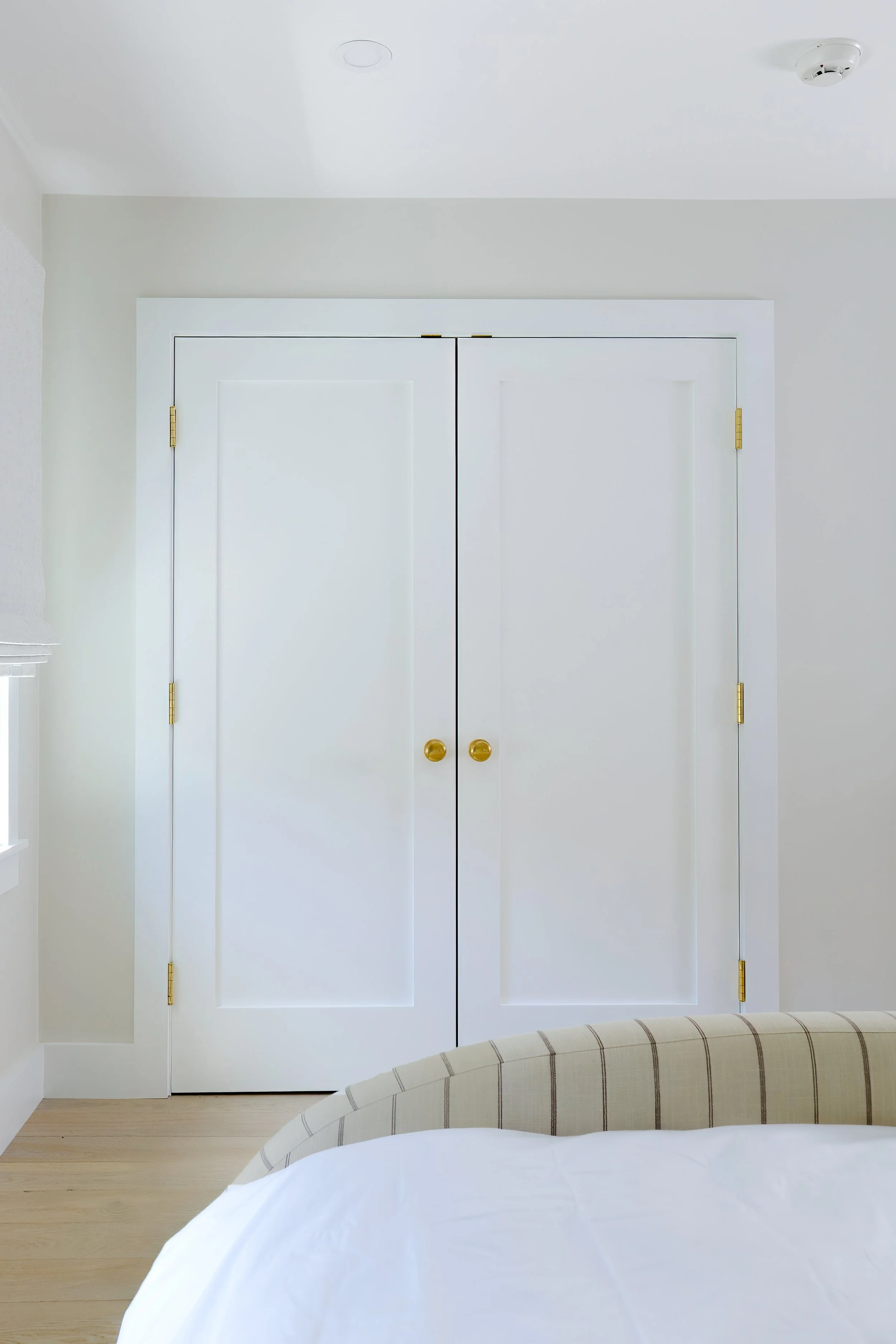 White closet doors with gold knobs and striped bed detail suit a coastal bedroom design.