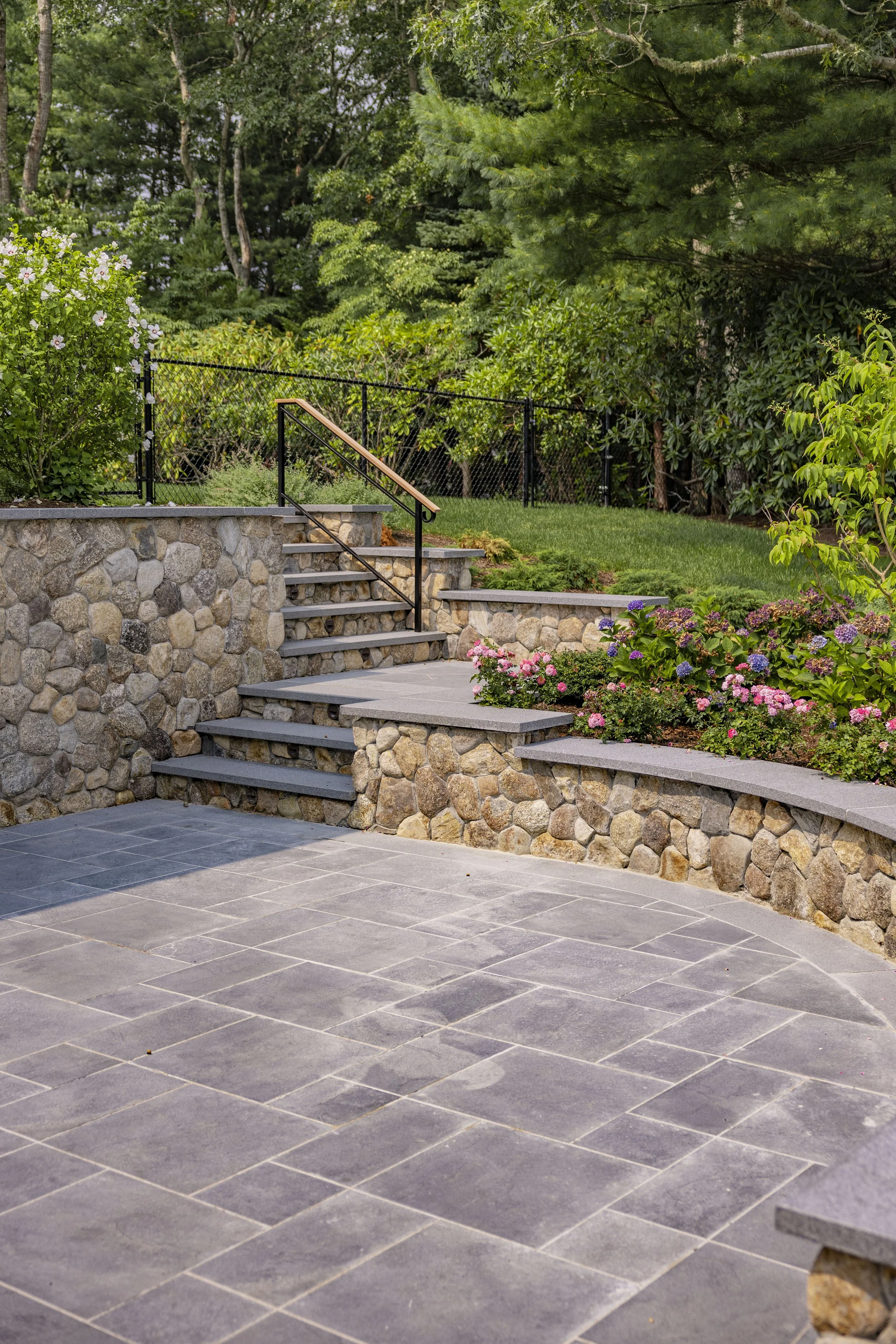 Stone patio and garden steps with flowering walls and wooded views at a Cape Cod property.