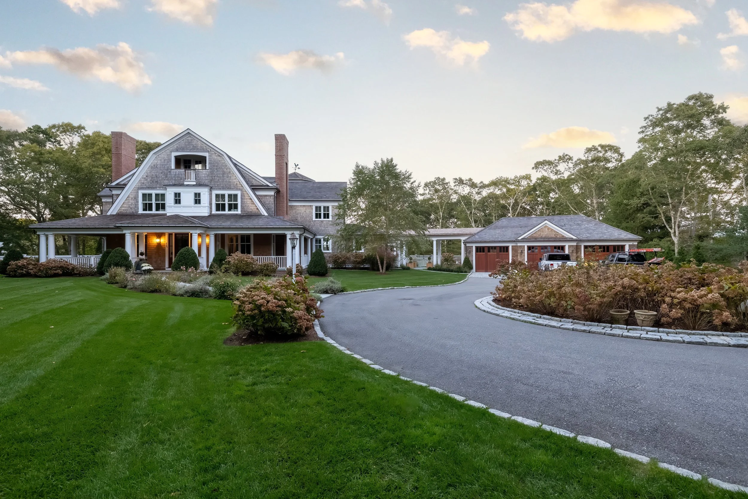 Cape Cod estate with shingled main house, circular driveway, detached garage, and expansive landscaped grounds.