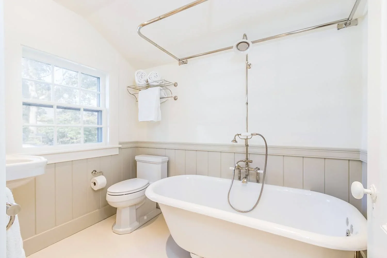 Cape Cod bathroom with a freestanding soaking tub, vintage-style shower, beadboard wainscoting, and abundant natural light..