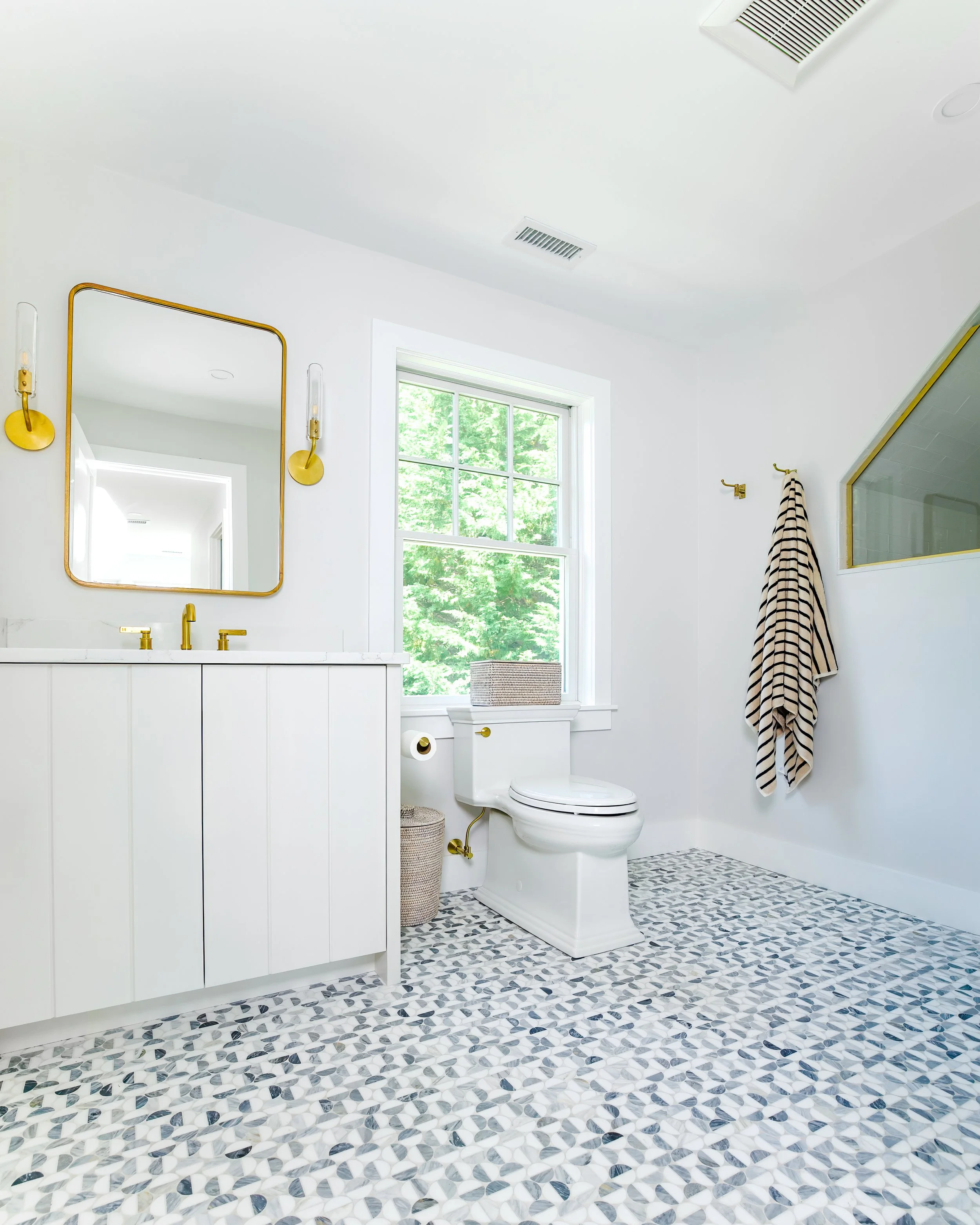 Gold fixtures, patterned tile, and a paneled vanity bring fresh coastal bathroom design to this space.