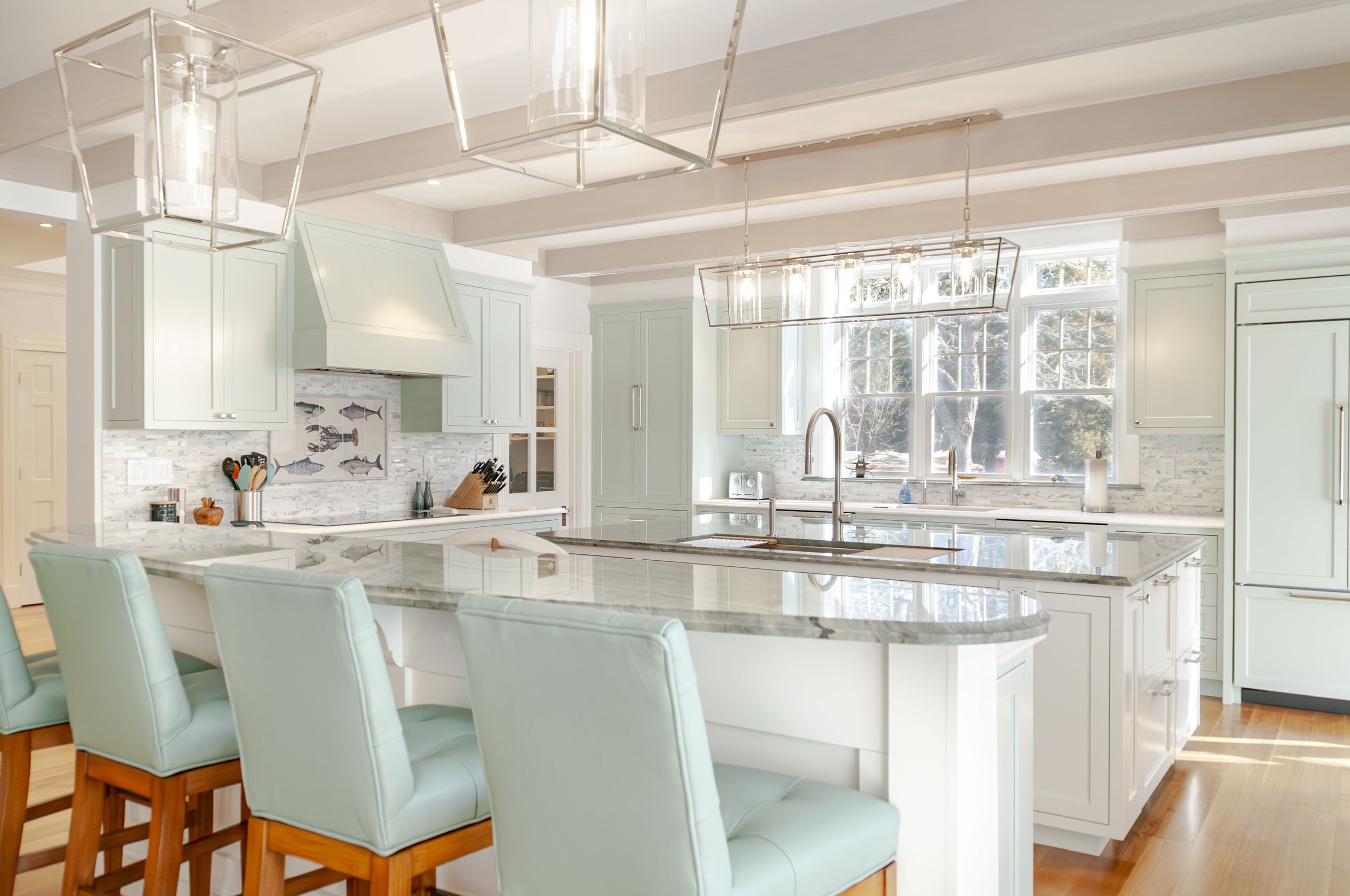 Open Cape Cod living space with soft green kitchen cabinetry, white sectional, pendant lights, and dining nook.