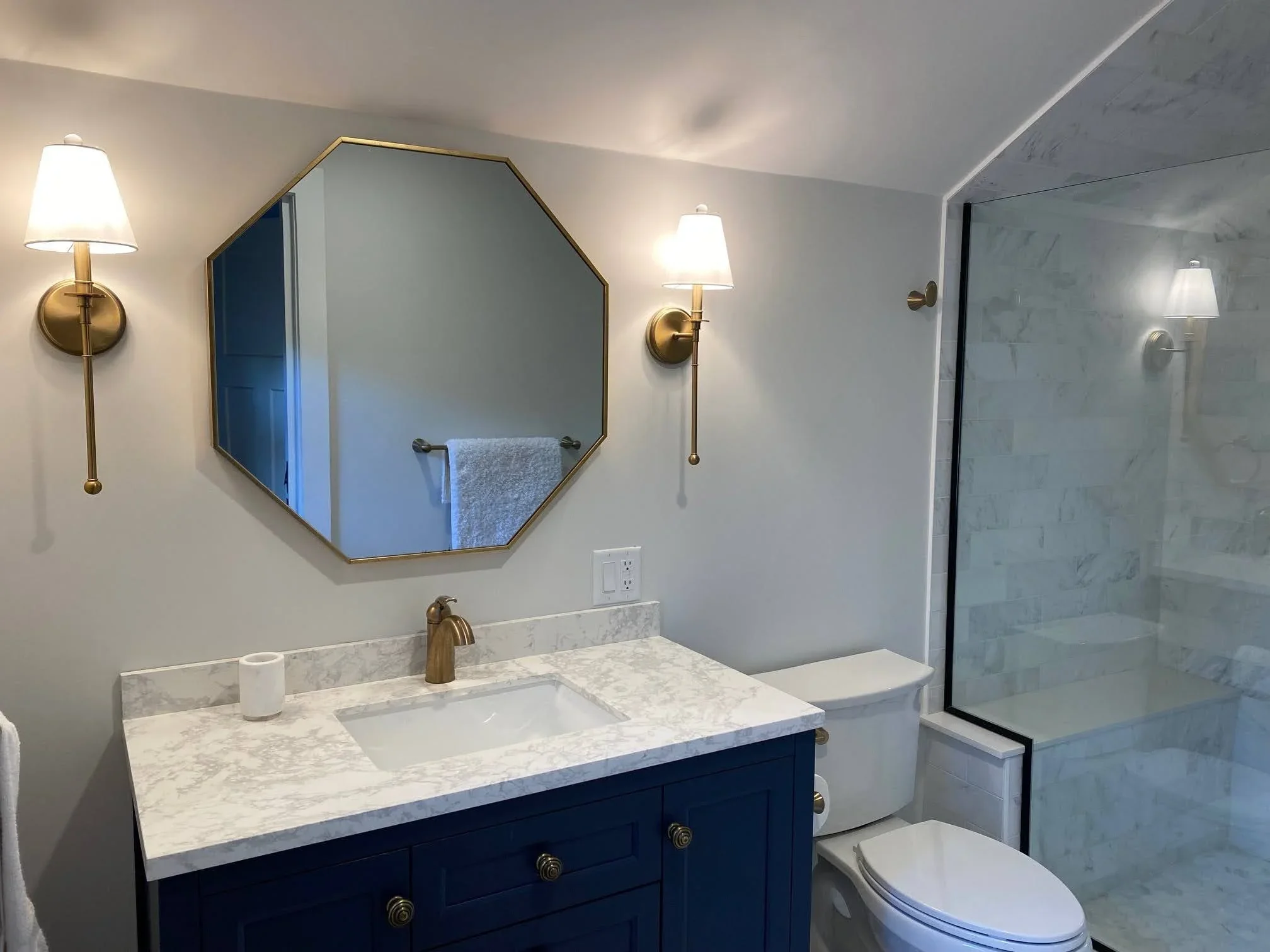 Sea View Builders designed this custom bathroom with a navy vanity, marble tile shower, quartz countertop, and timeless Cape Cod coastal design.