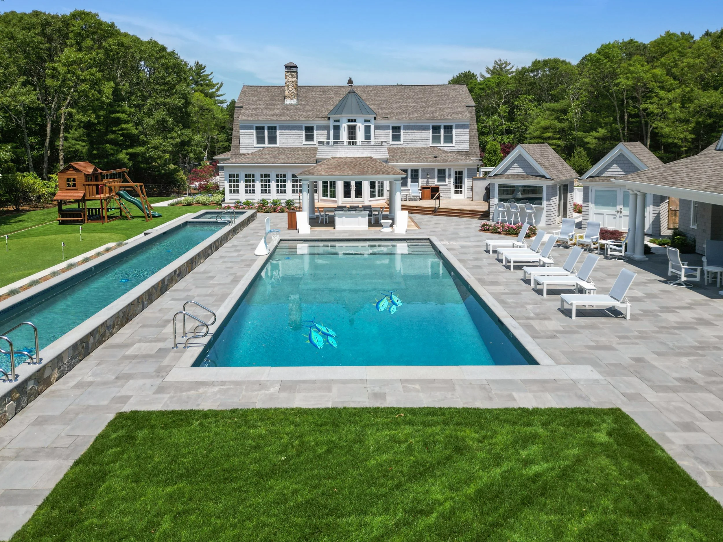 Custom coastal home with pool terrace, lap pool, cabanas, lounge seating, and surrounding trees.