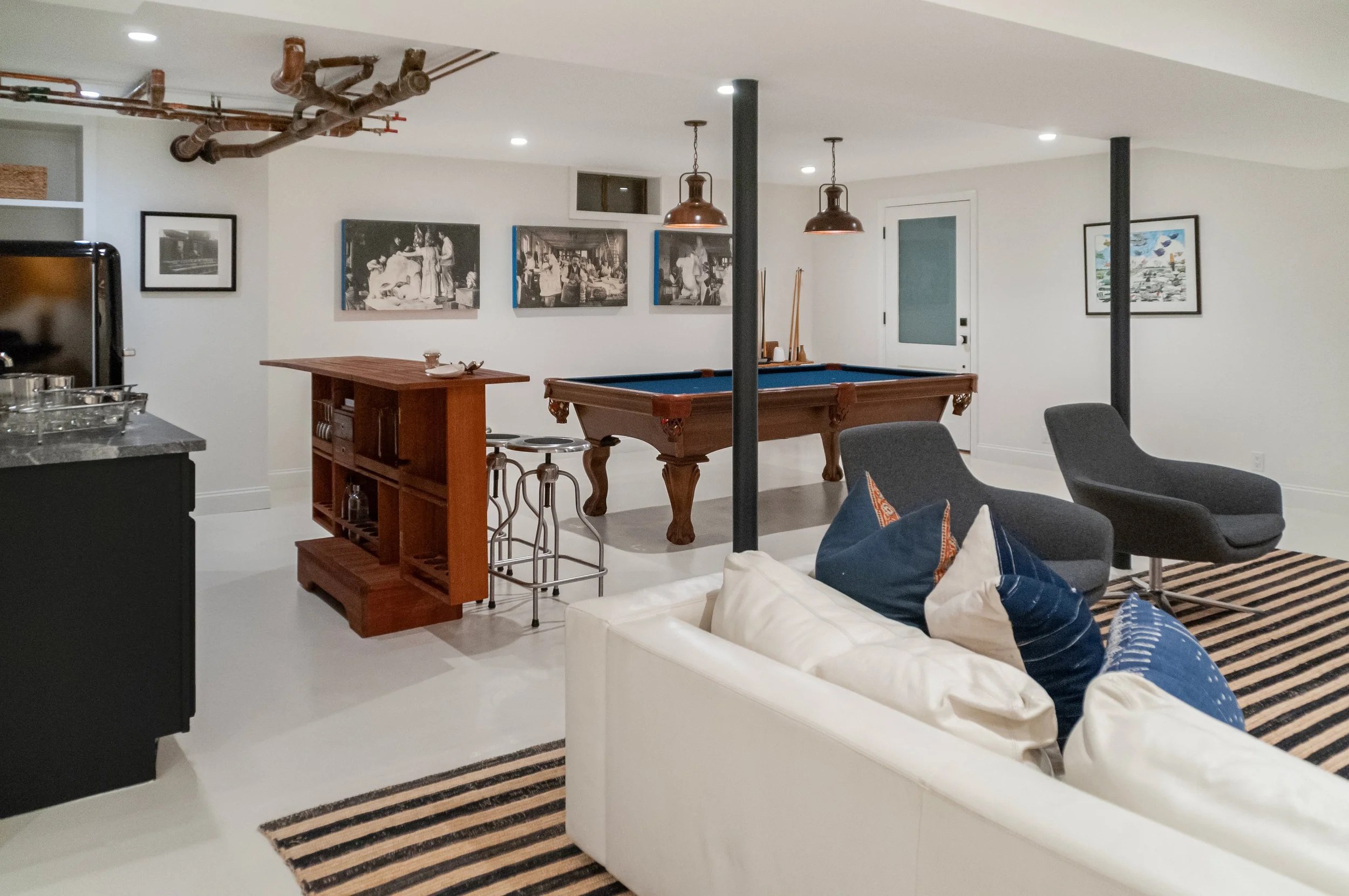 Lower-level lounge with white sectional, striped rug, navy pillows, and Cape Cod entertaining space style.