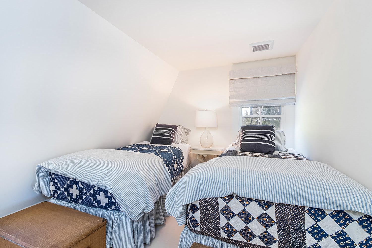 Twin beds with patterned quilts and striped bedding create a cozy Cape Cod cottage guest room.