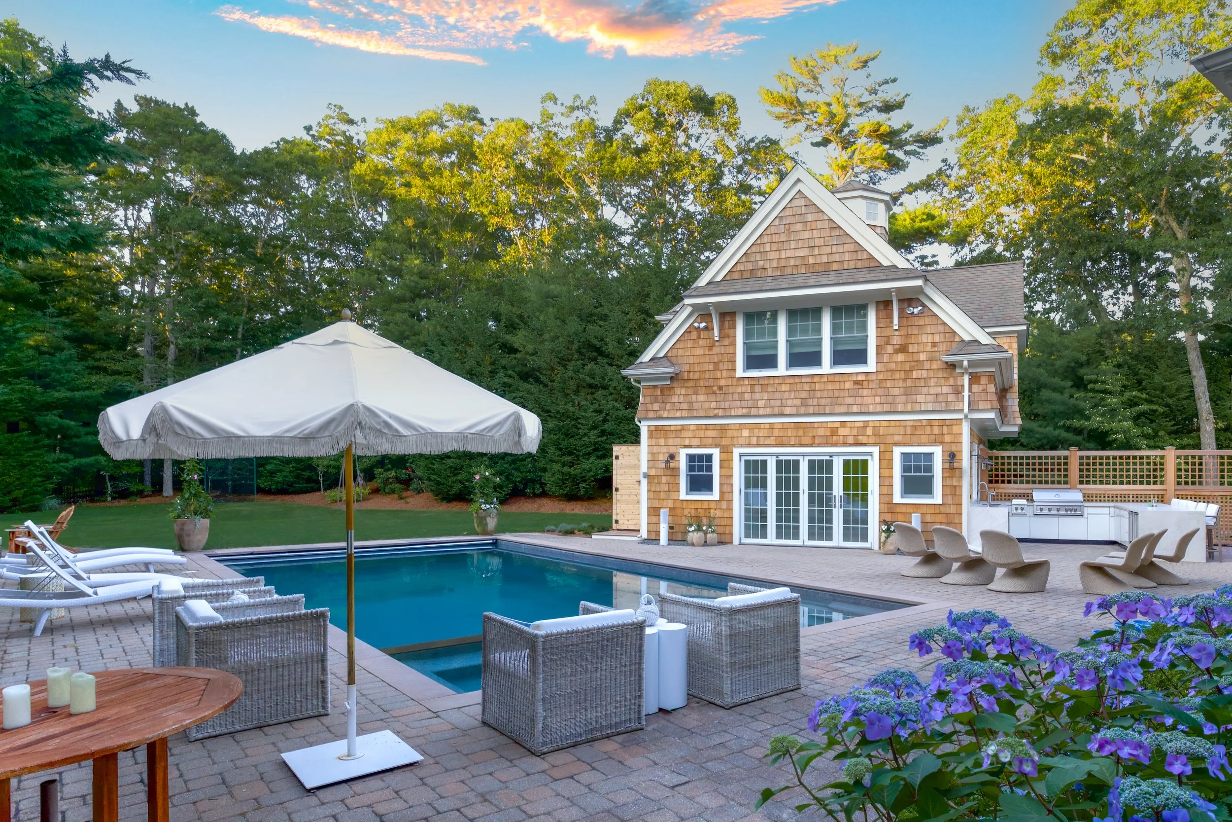 Poolside patio with pool house, umbrella seating, hydrangeas, and Cape Cod outdoor living appeal.