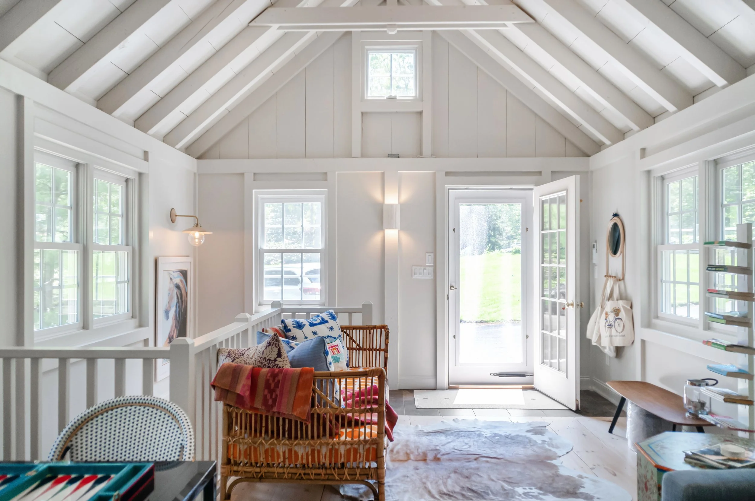 Bright vaulted entry sitting area with paneled walls, exposed beams, and an open glass door.