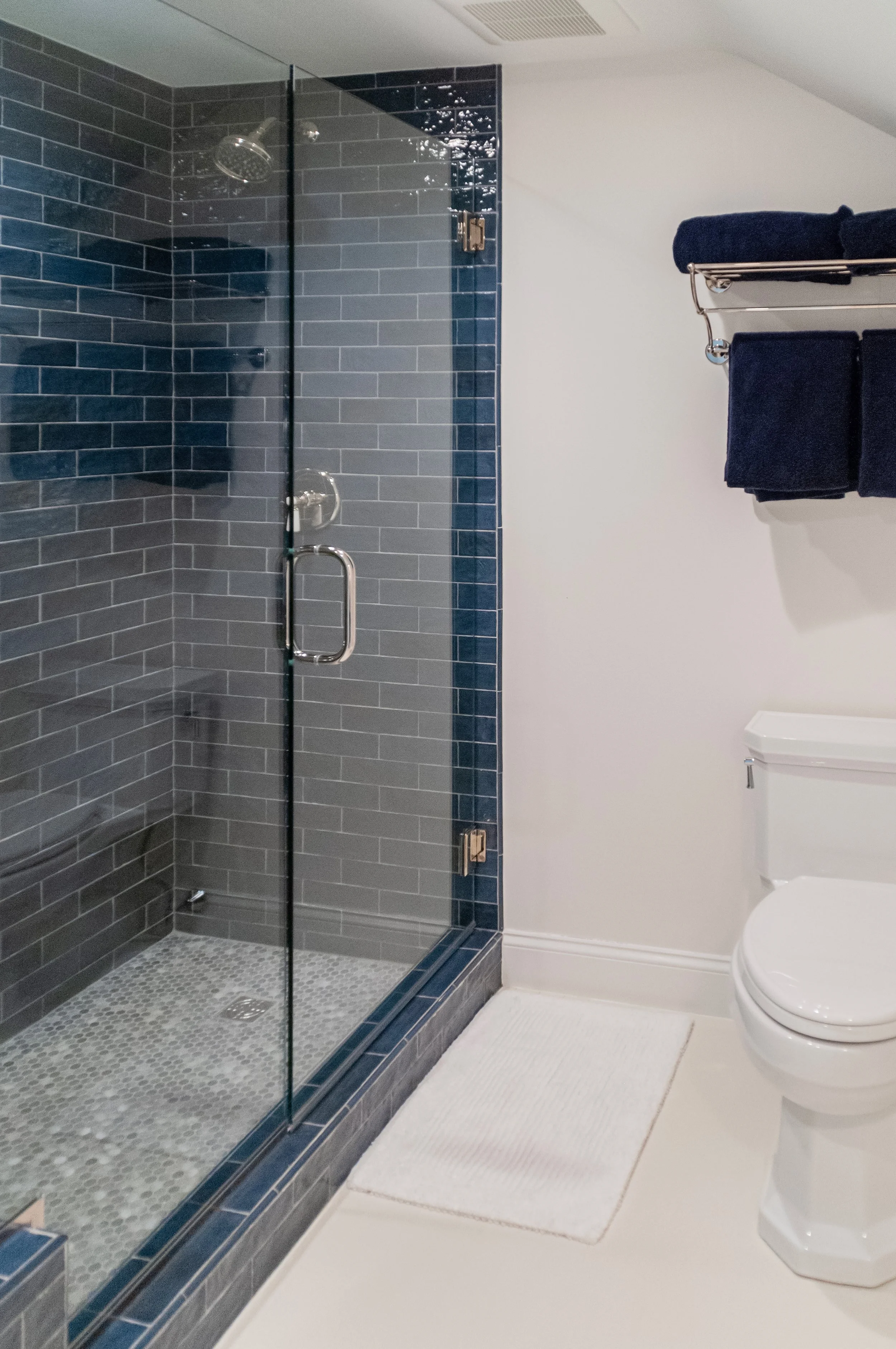 Glossy blue tile and a glass shower give this custom coastal home bath a tailored Cape Cod finish.