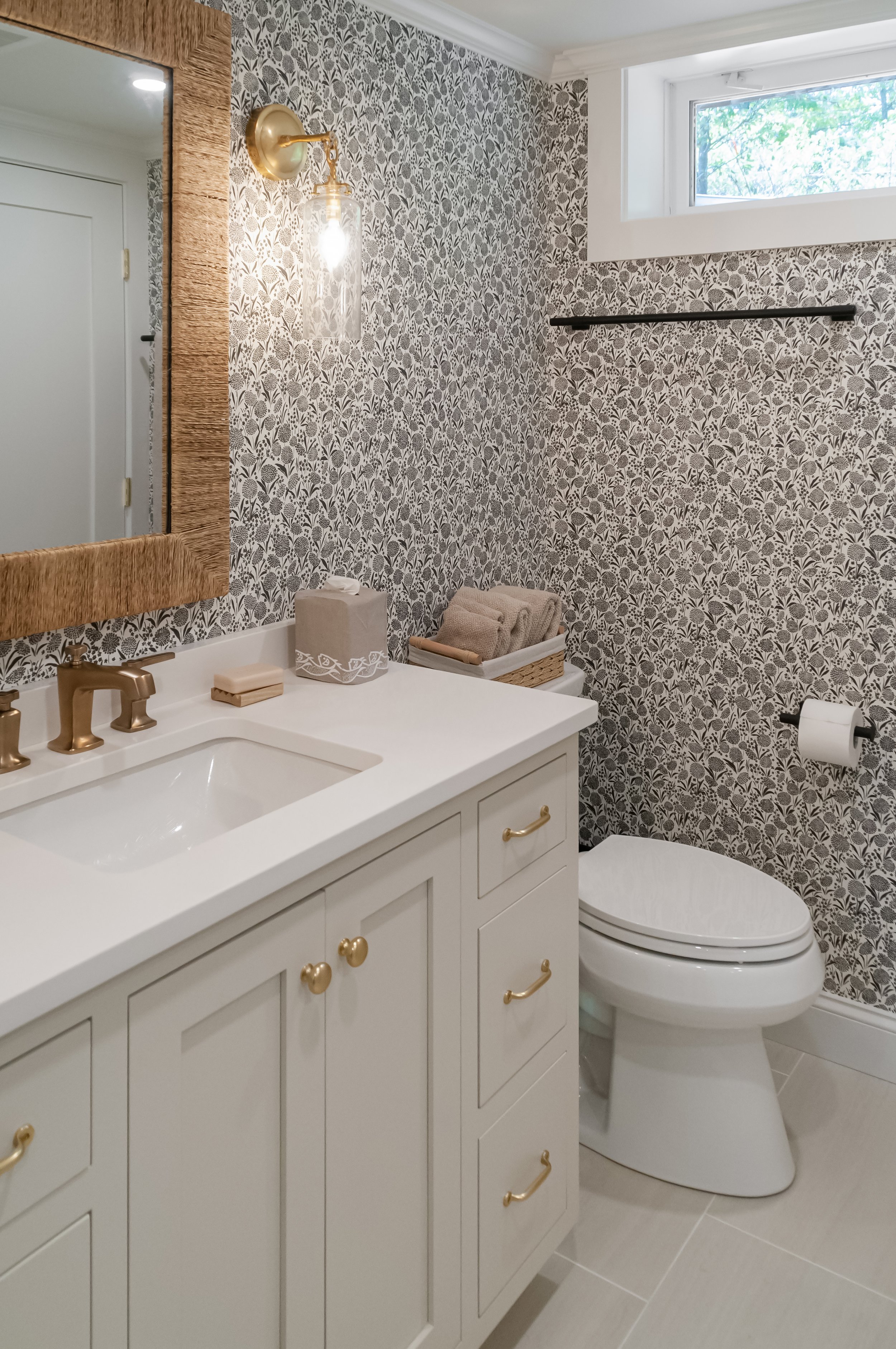 Soft patterned wallpaper and brass accents bring high-end Cape Cod renovation style to this compact powder bath.