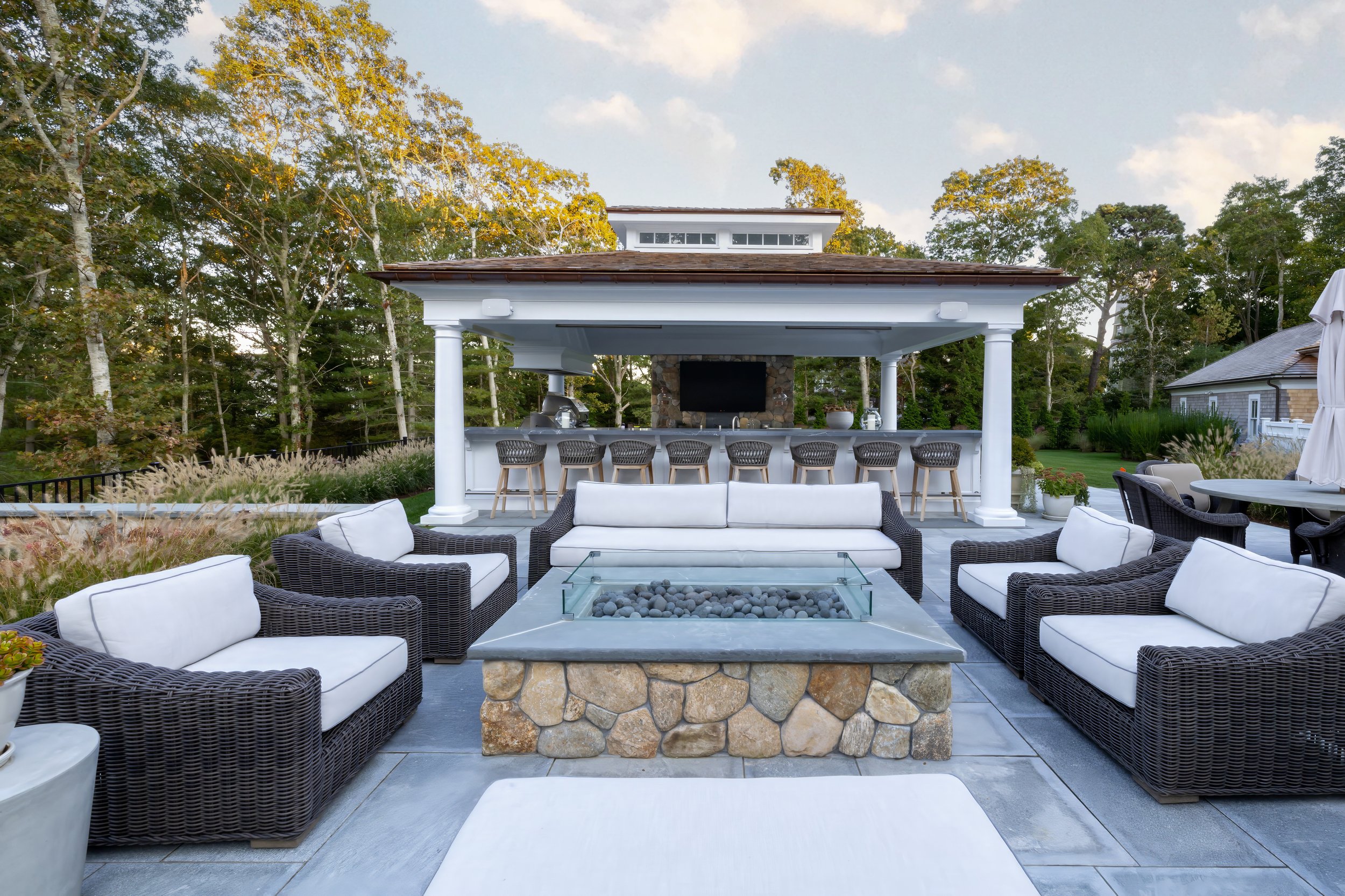 Sea View Builders designed this Cape Cod backyard with a custom pool house, outdoor kitchen, fire pit, covered seating, and luxury outdoor entertaining area.