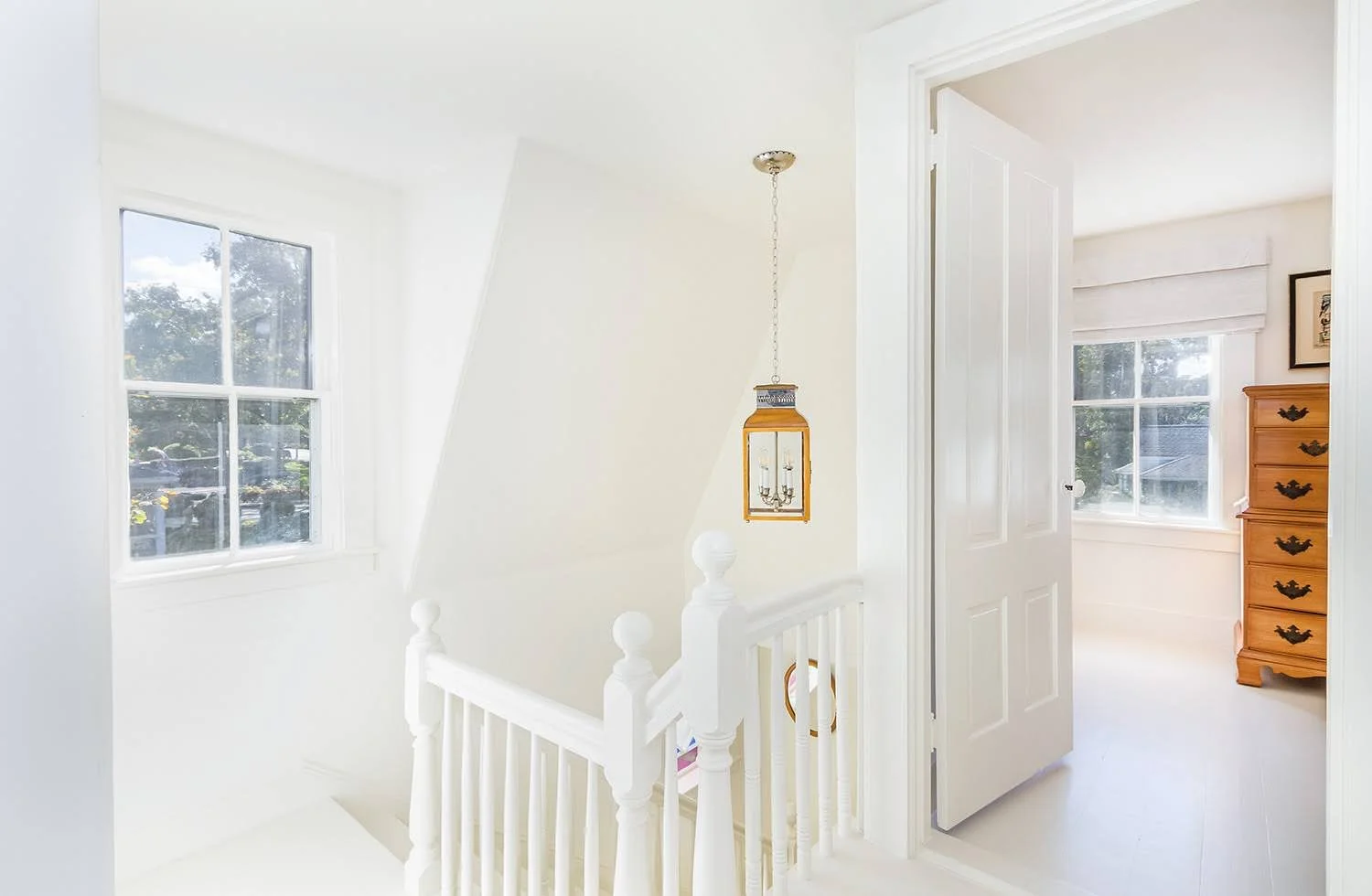Bright white entryway with stair railing and round mirror adds classic Cape Cod cottage charm.