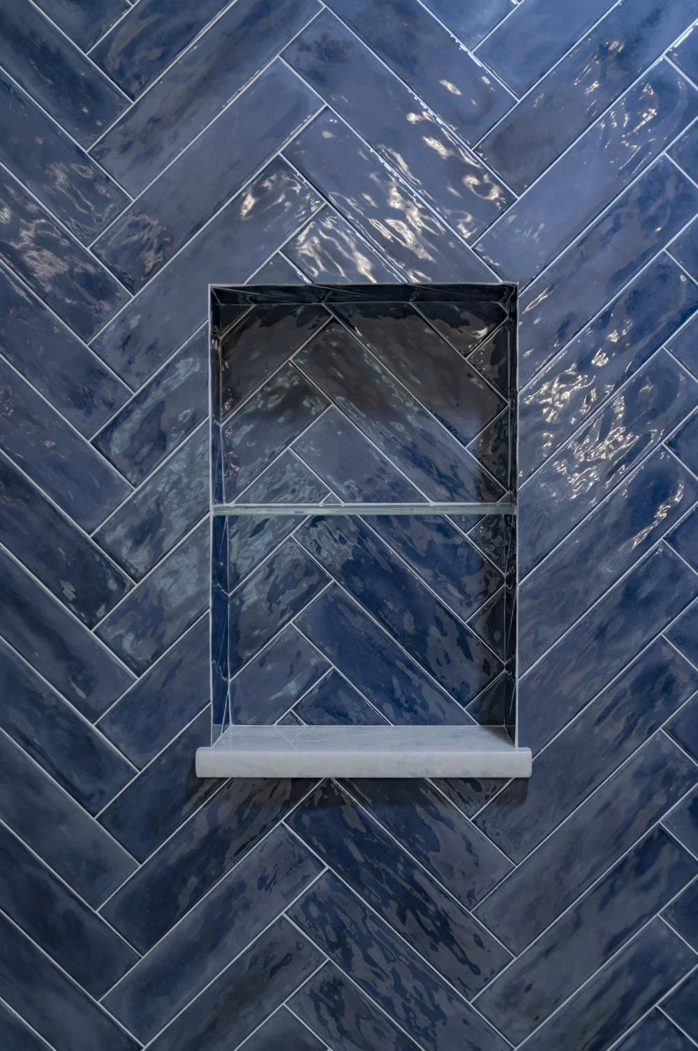 Glossy blue shower niche and herringbone tile add custom coastal home detail to this Cape Cod bath.
