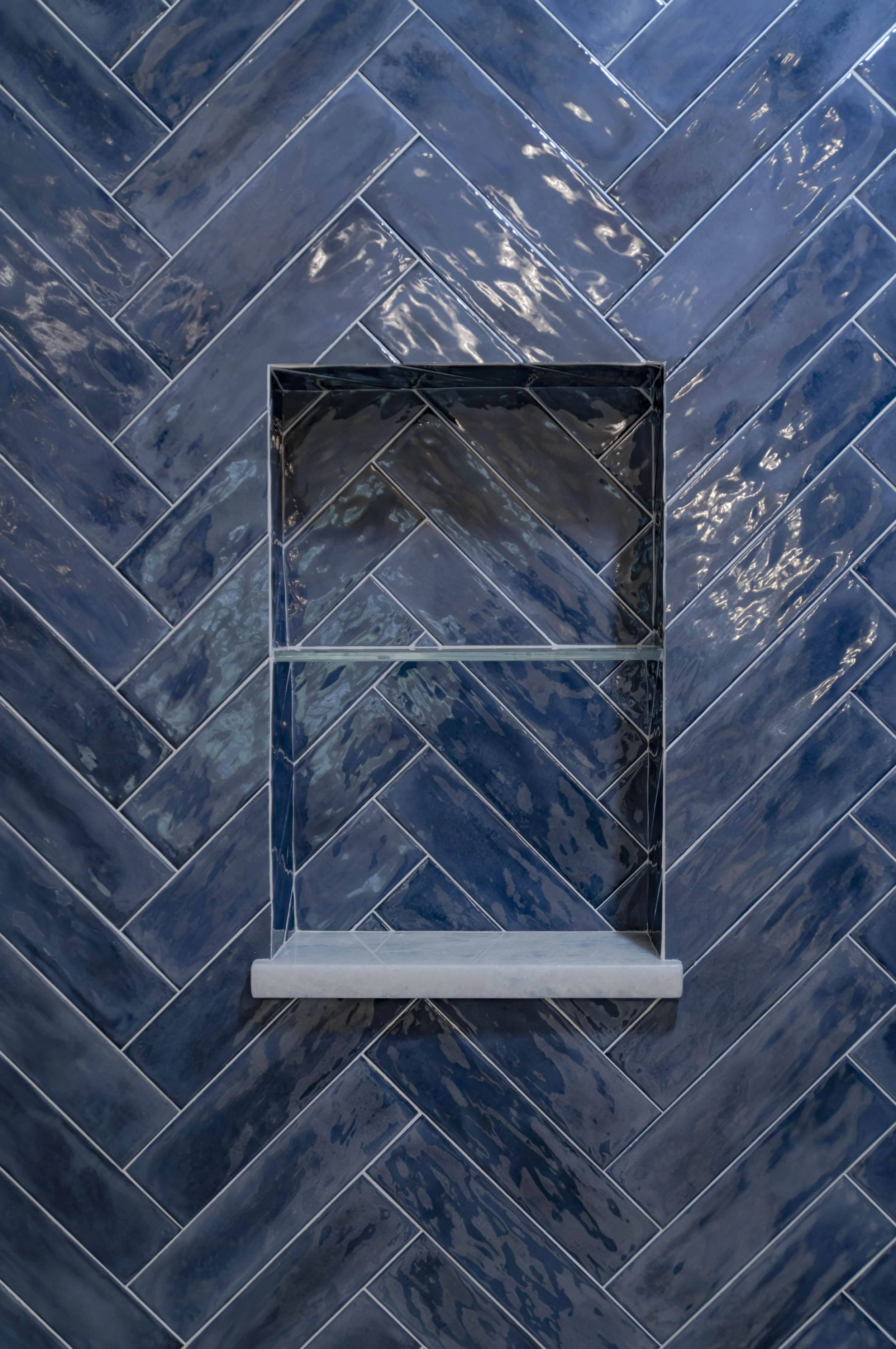 Cape Cod shower with glossy blue herringbone tile, marble shelf, and polished detailing.