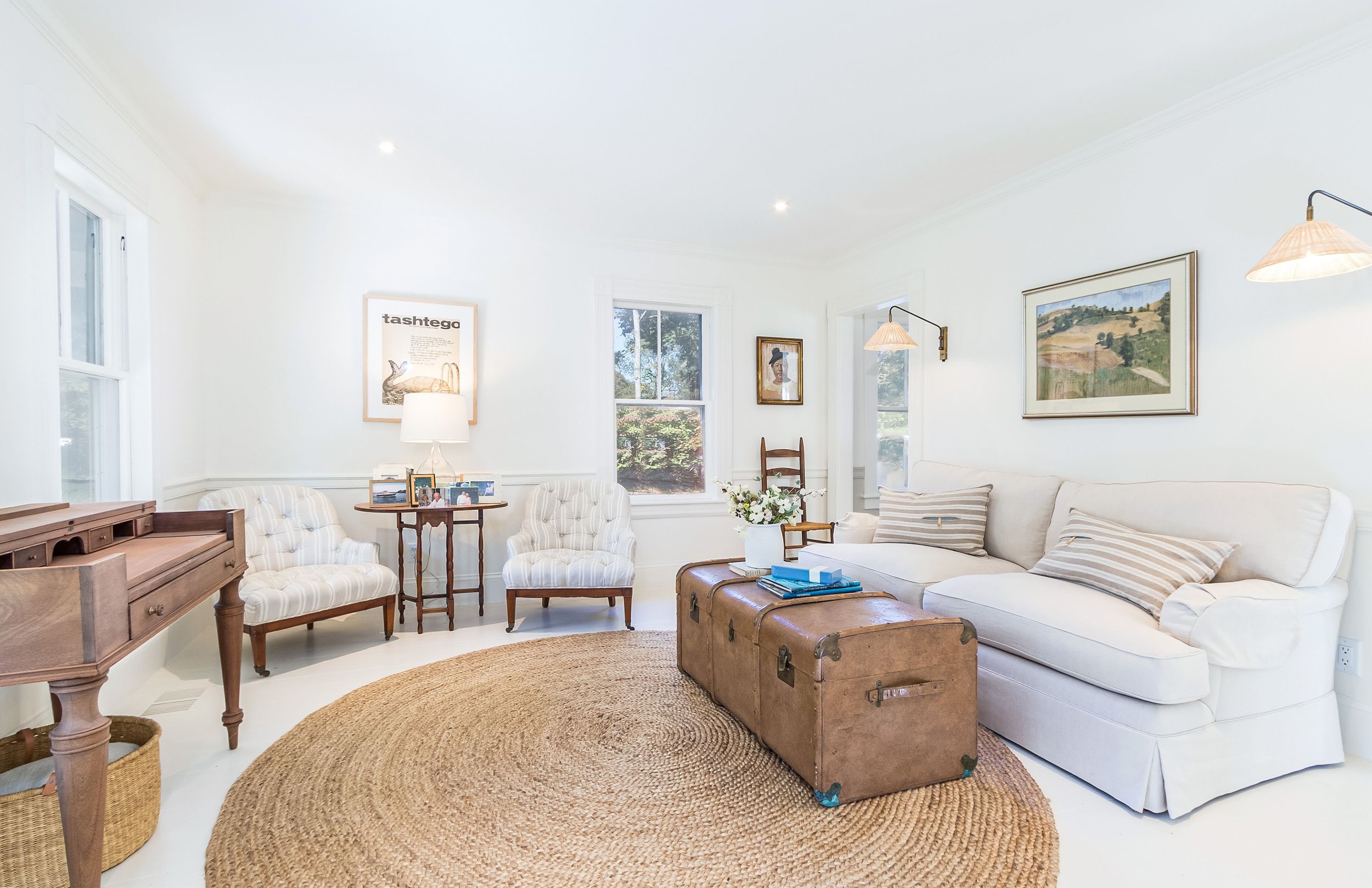 White sitting room with skirted sofa, antique trunk, piano, and bright Cape Cod cottage interior style.