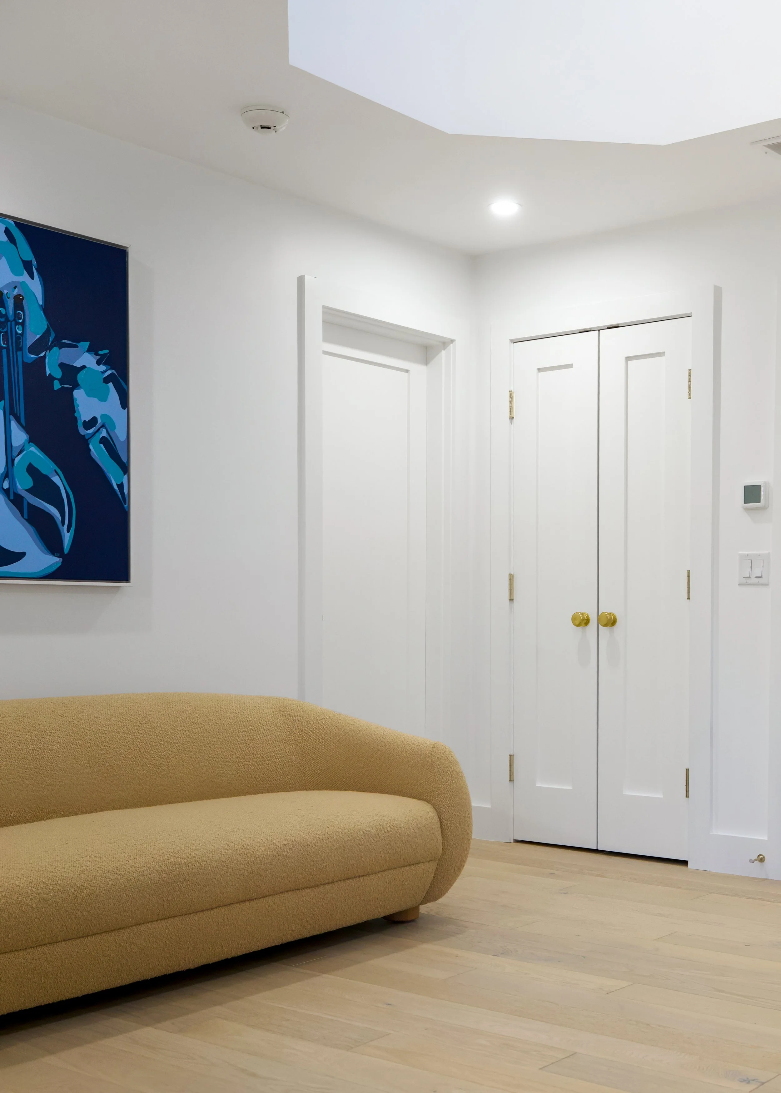 Curved sofa, white doors, brass hardware, and bold artwork define this modern coastal interior.