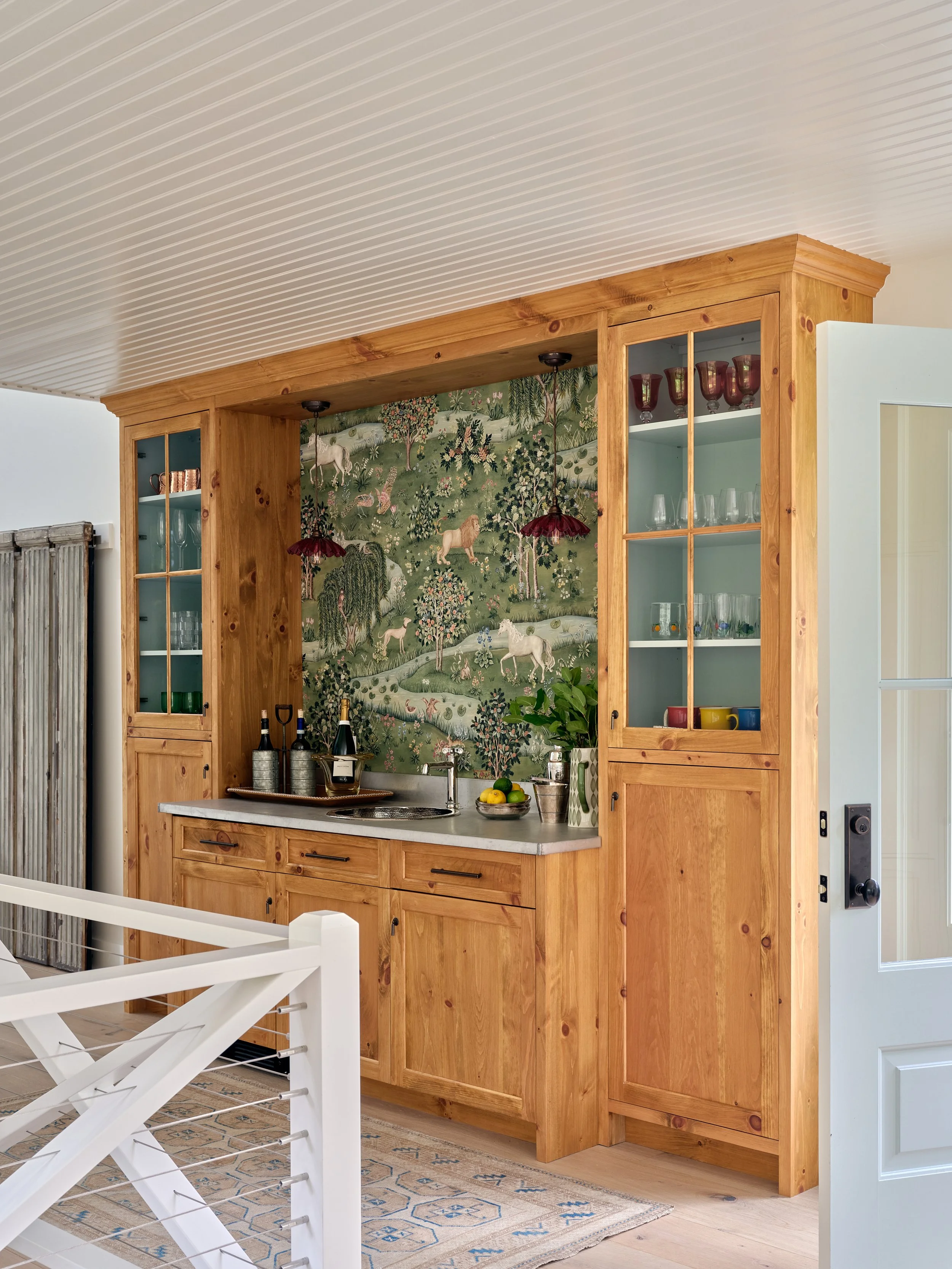 Framed by custom wood cabinetry, this Sea View Builders wet bar features a built-in beverage station, stone countertop, glass display cabinets, and timeless Cape Cod design.